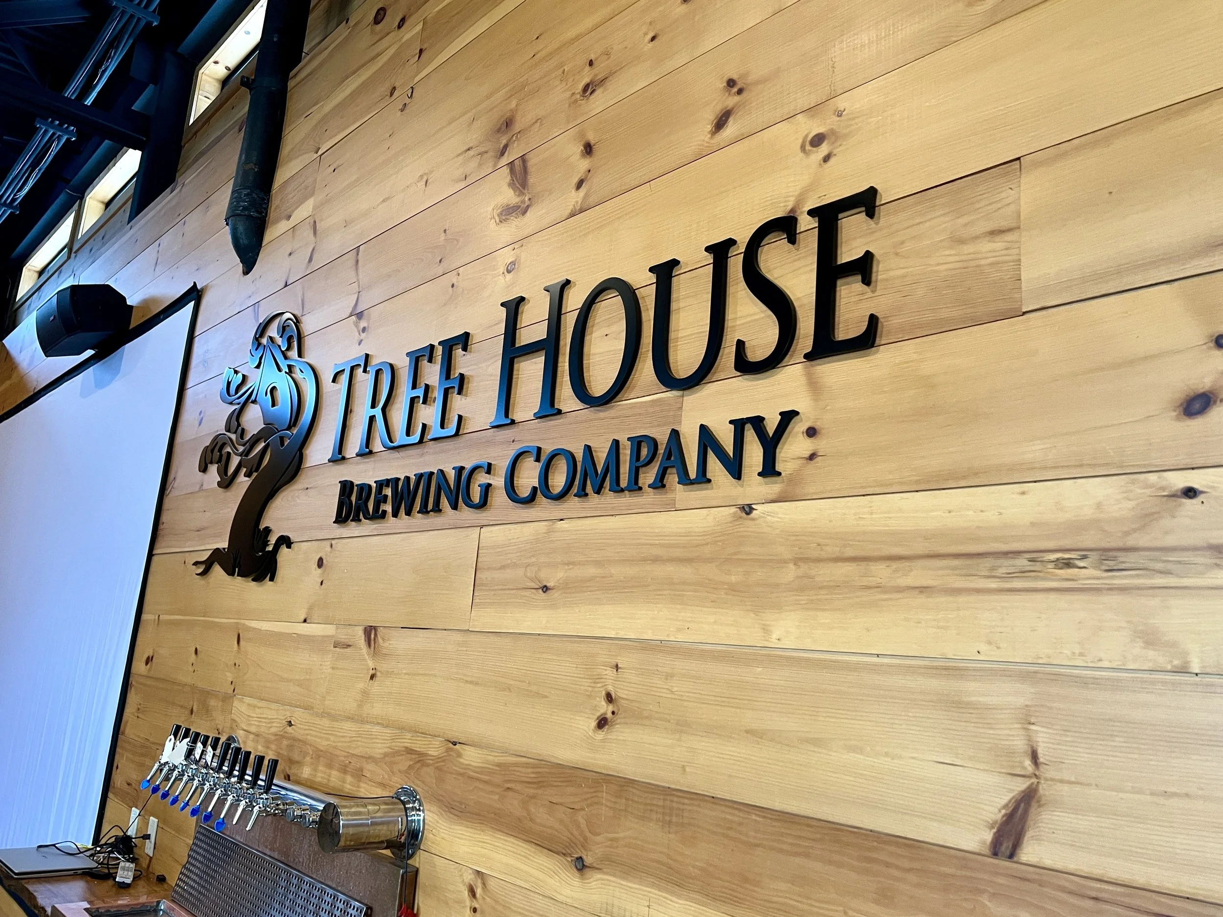 Rustic wood wall sign reading “Tree House Brewing Company” above a row of beer taps.
