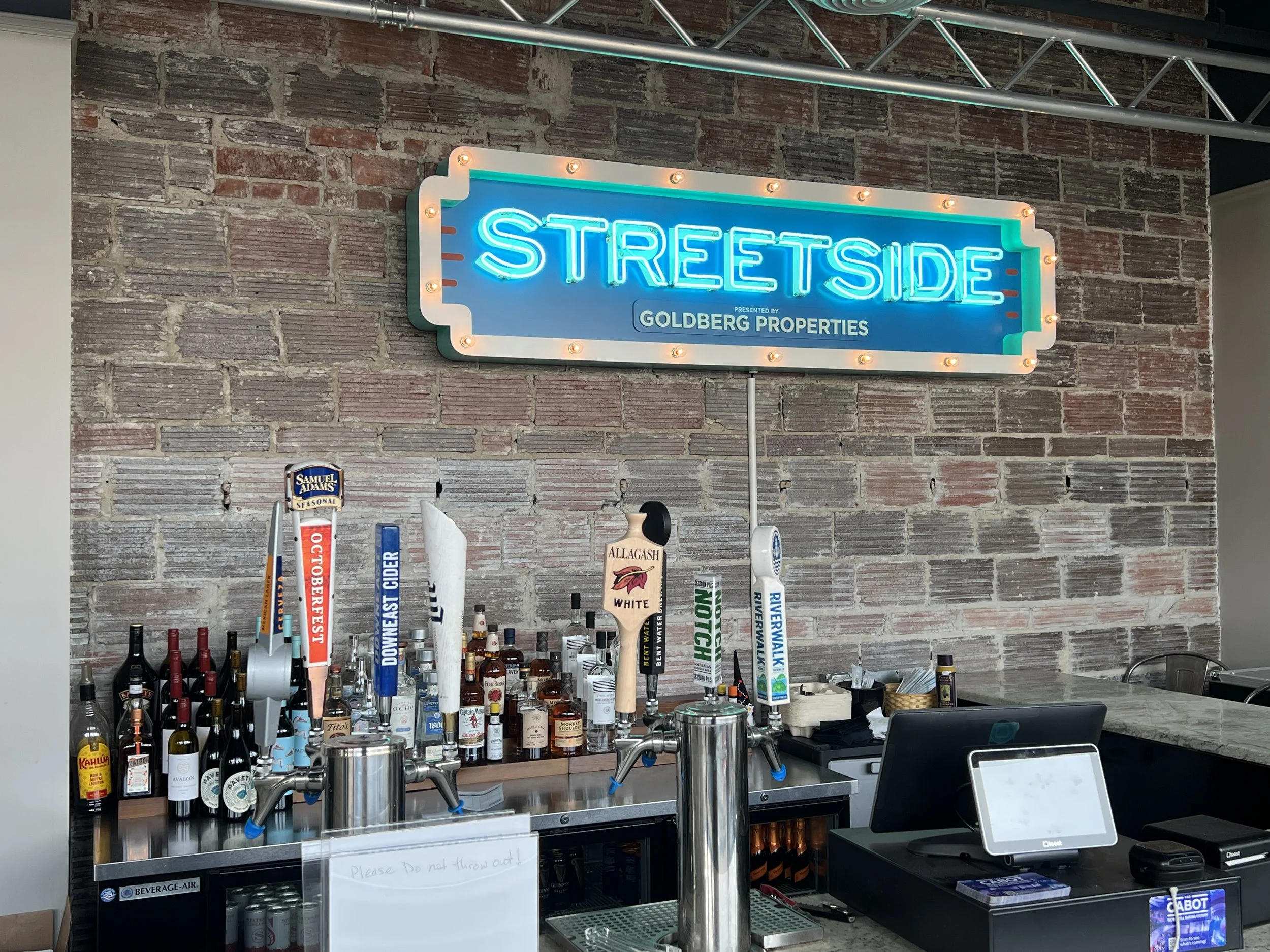 Bar with liquor bottles, beer taps, and a neon "STREETSIDE" sign on a brick wall