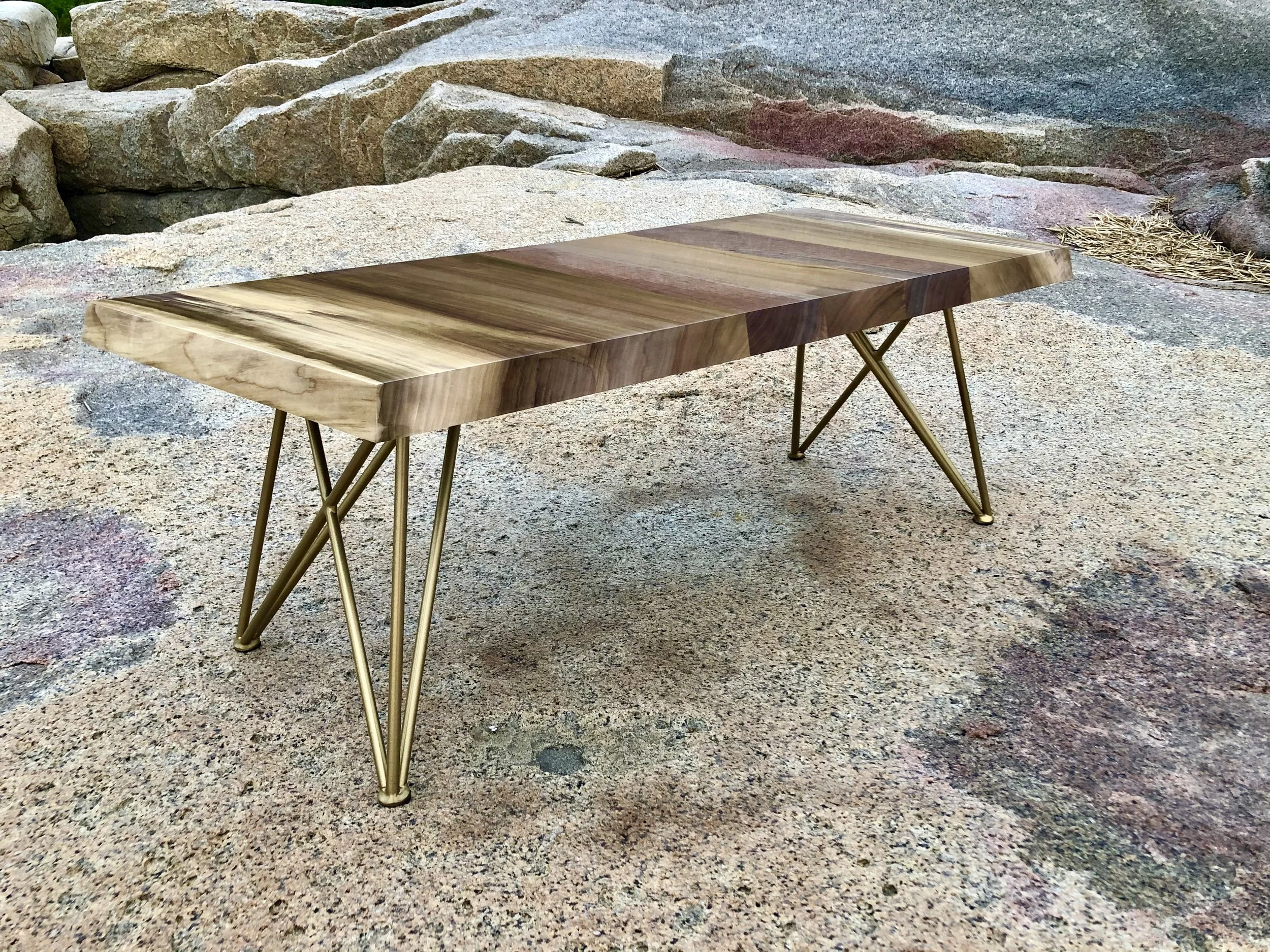 Live-edge walnut dining table with gold hairpin legs displayed outdoors on granite rocks