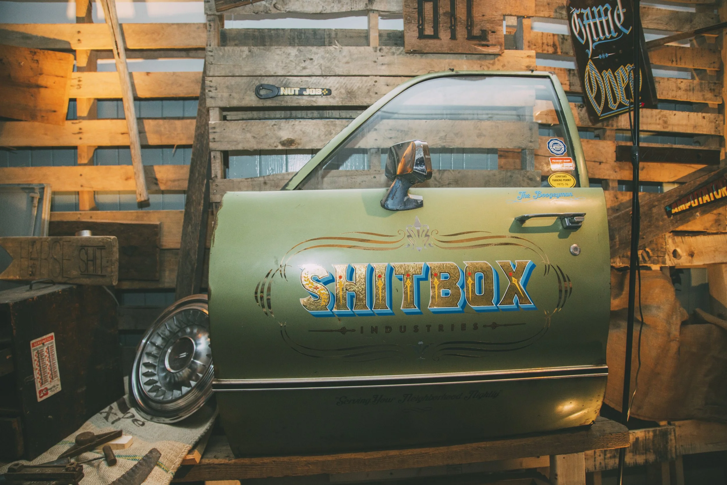 Vintage green Volkswagen Shitbox Industries car door displayed in a rustic wooden workshop