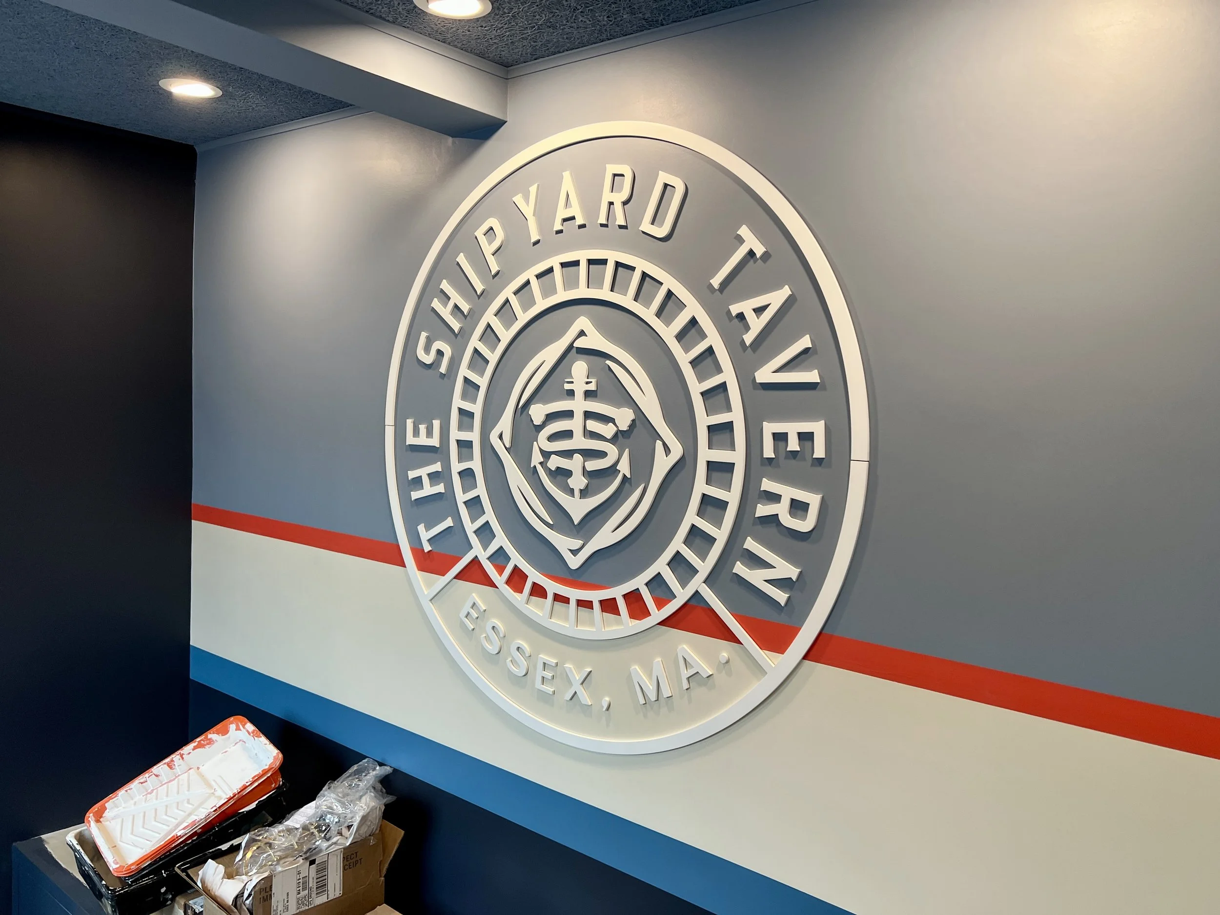 Large circular Shippard Fitness Academy wall logo with a central muscular figure, red and blue stripes, and ceiling lights