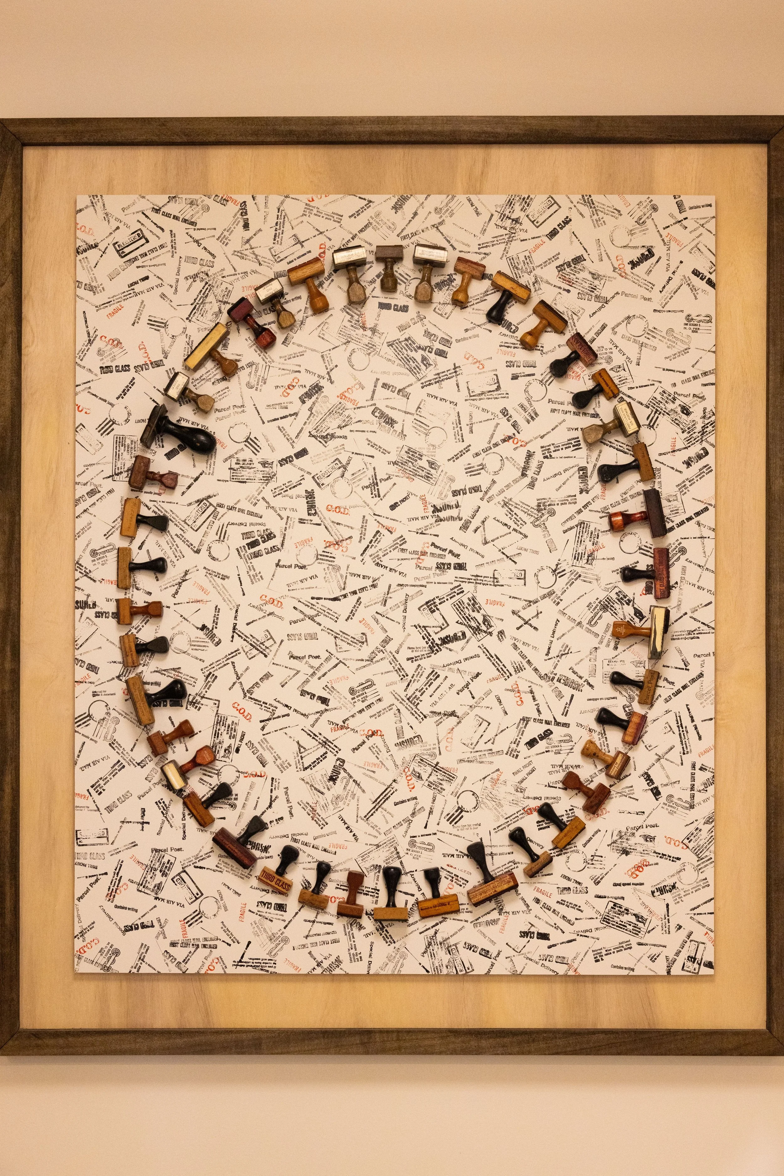 Framed artwork featuring vintage postal rubber stamps scattered across a collage of mail and parcel markings.