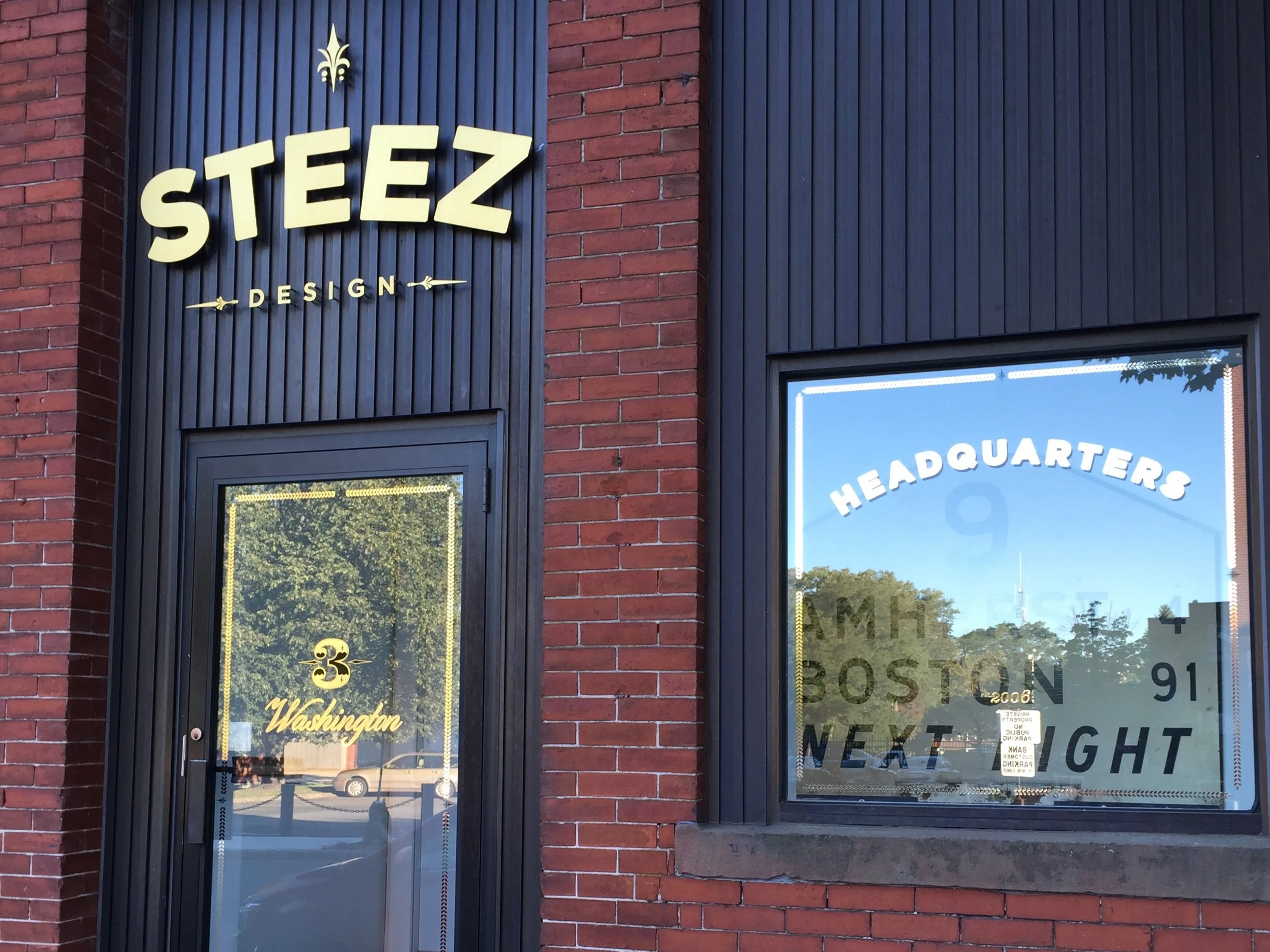 Exterior of STEEZ Design headquarters in Boston, with a red brick facade, black siding, and gold signage.