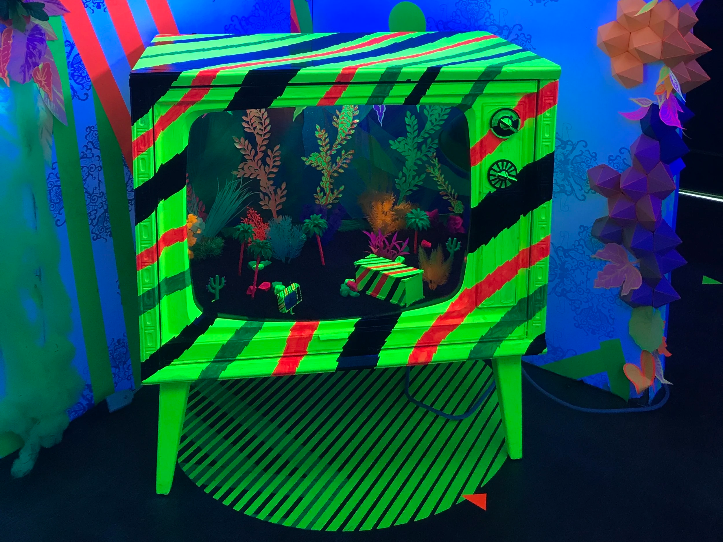Neon green and red striped aquarium display filled with colorful artificial aquatic plants and rocks