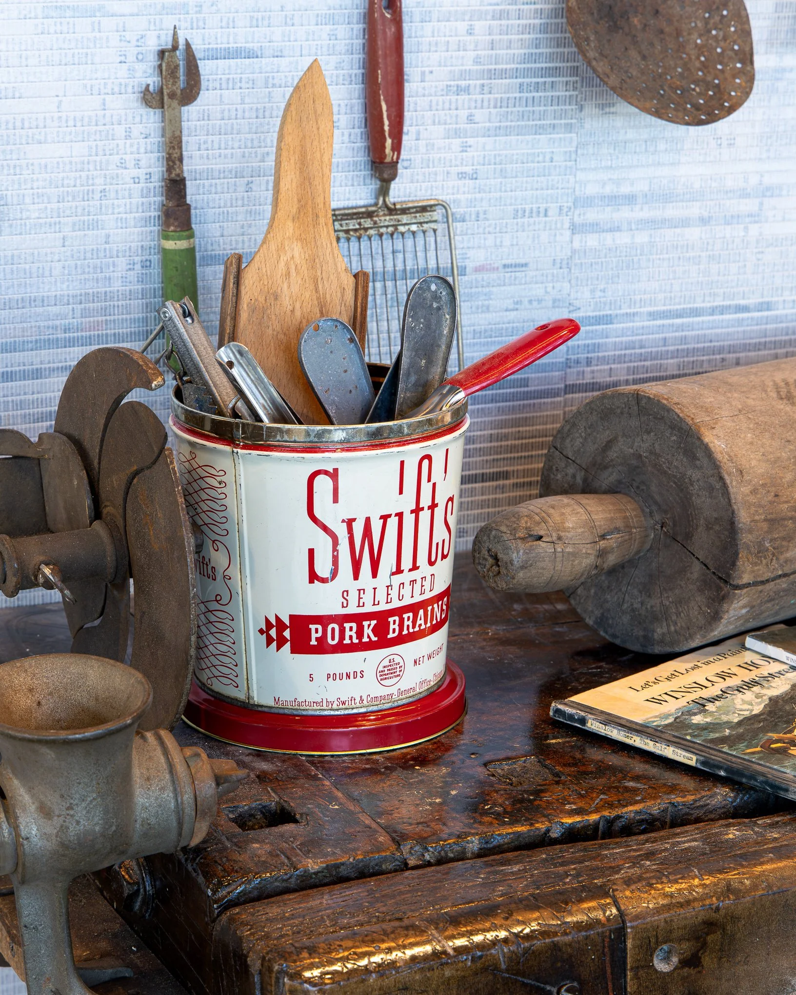 Vintage kitchen utensils in a Swift's pork brains tin on a rustic wooden workbench