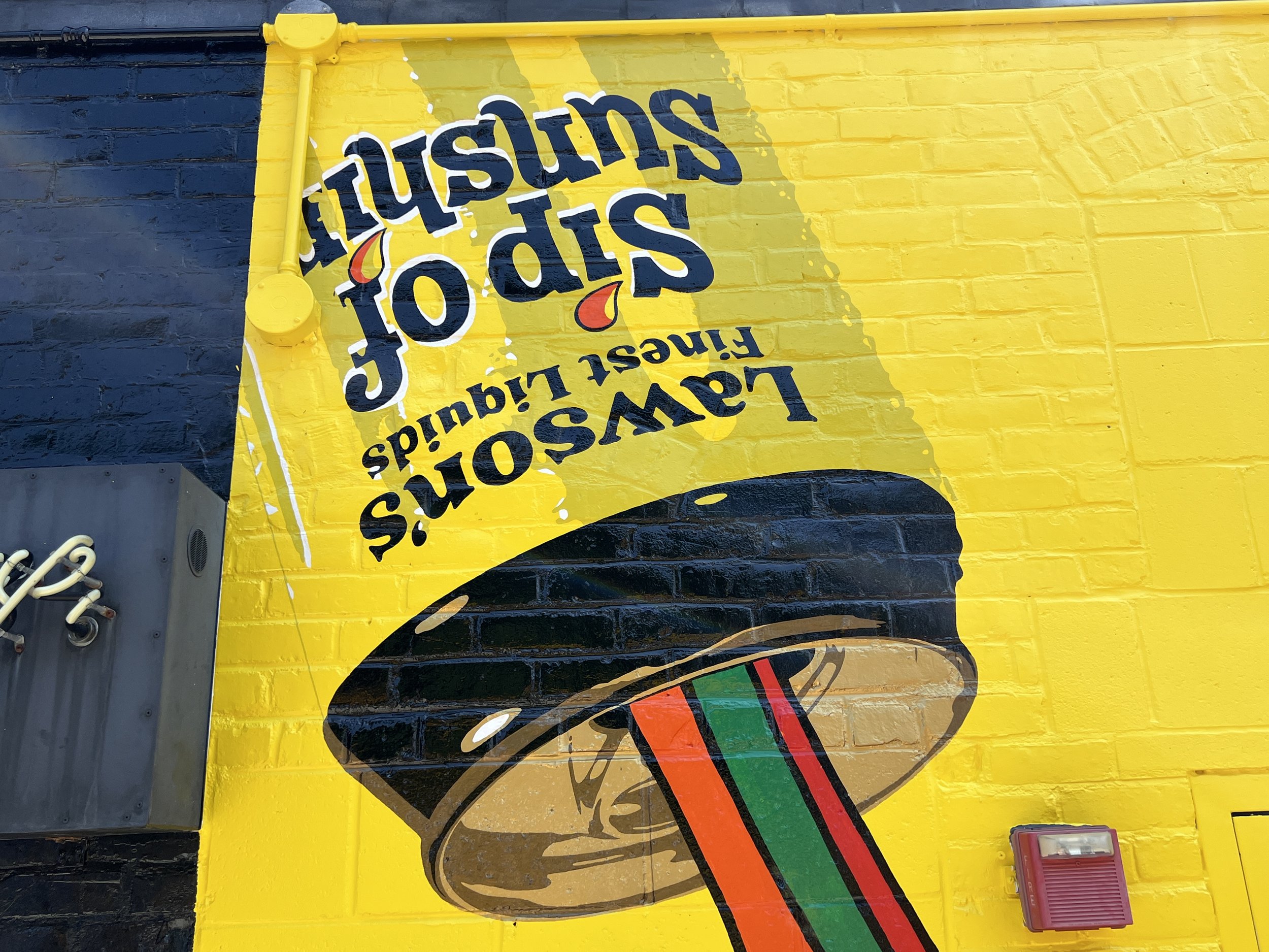 Colorful yellow mural featuring a smiling taco and the text “Tacos al pastor,” with red, green, and black accents.