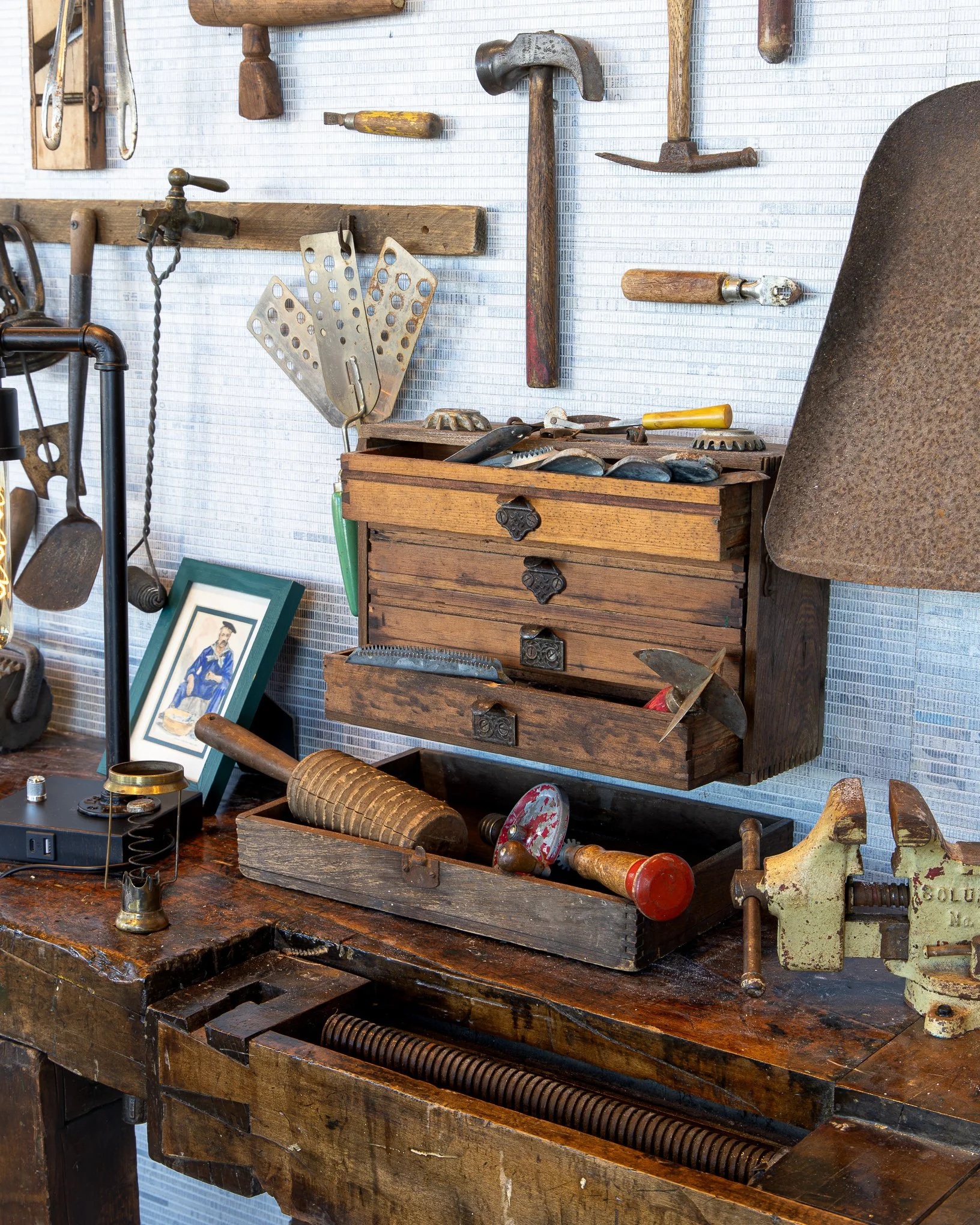 Vintage woodworking workshop with antique hand tools, hammers, saws, drill bits, wooden tool chests, and a large workbench.