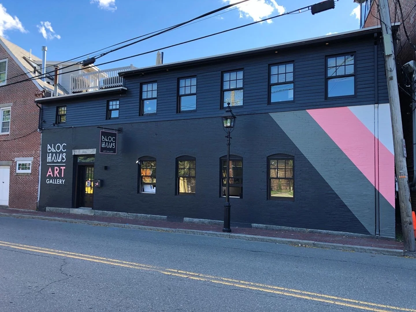 Black-painted Bloc Haus Art Gallery building with pink and gray geometric mural, storefront windows, and streetlamp.