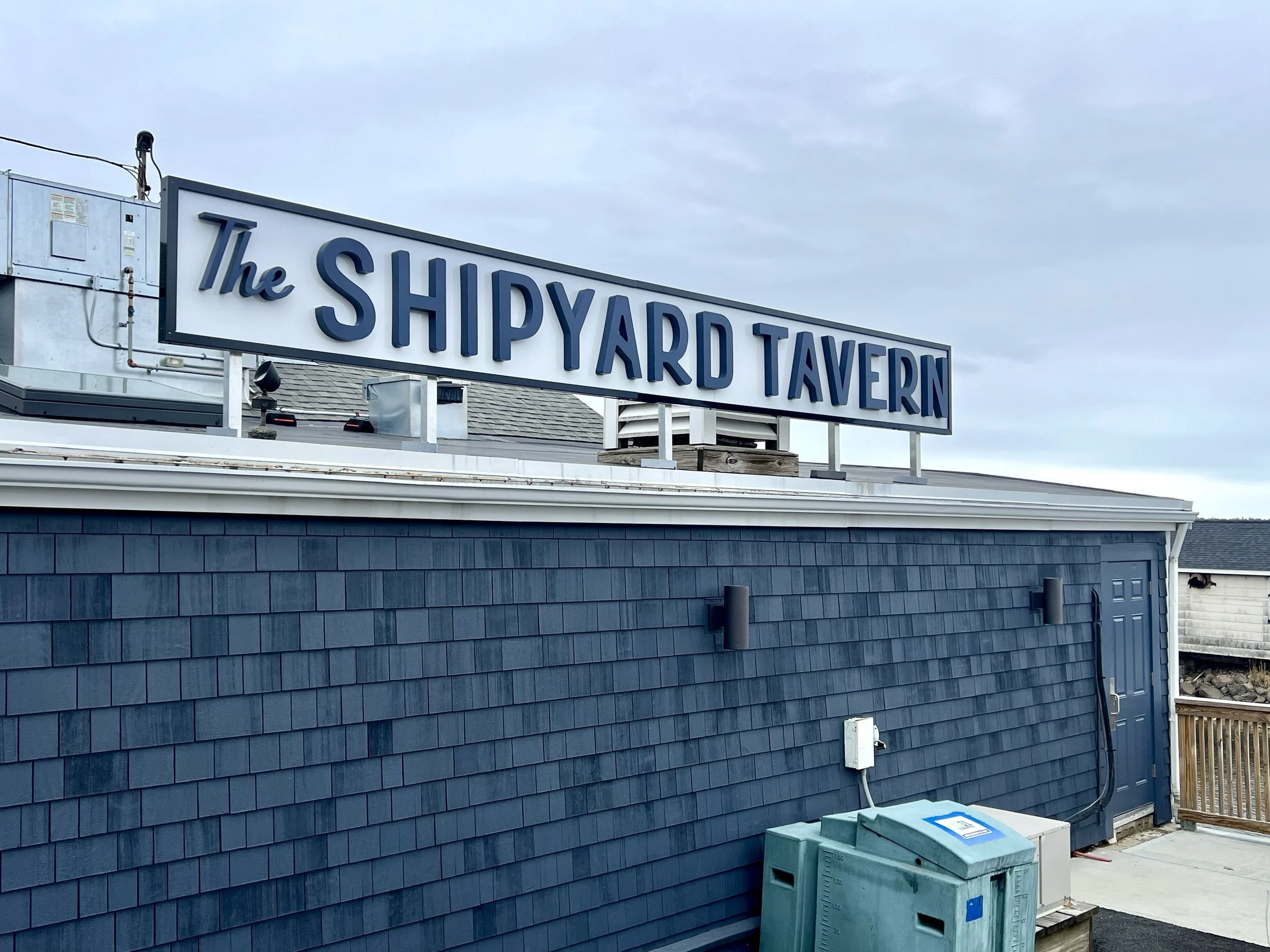 Rooftop sign reading “The Shipyard Tavern” on a blue-shingled building.