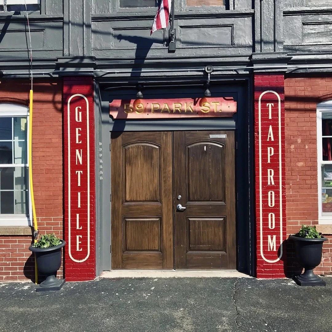 Red brick storefront entrance with wooden double doors, vintage signs reading “GENTILE” and “TAPROOM,” and “59 PARK ST.”