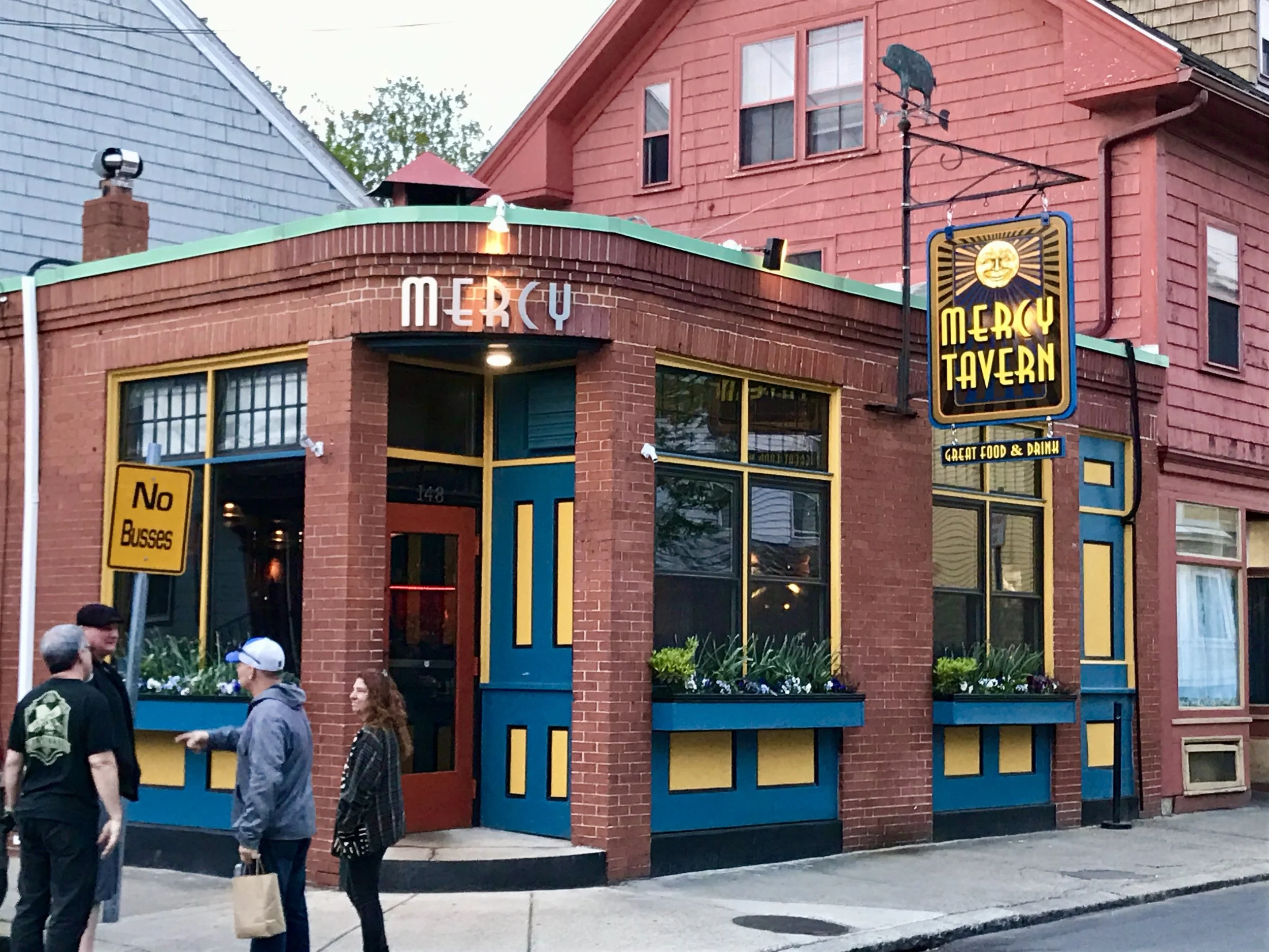 Exterior of Mercy Tavern with colorful brick facade, hanging sign, and pedestrians outside