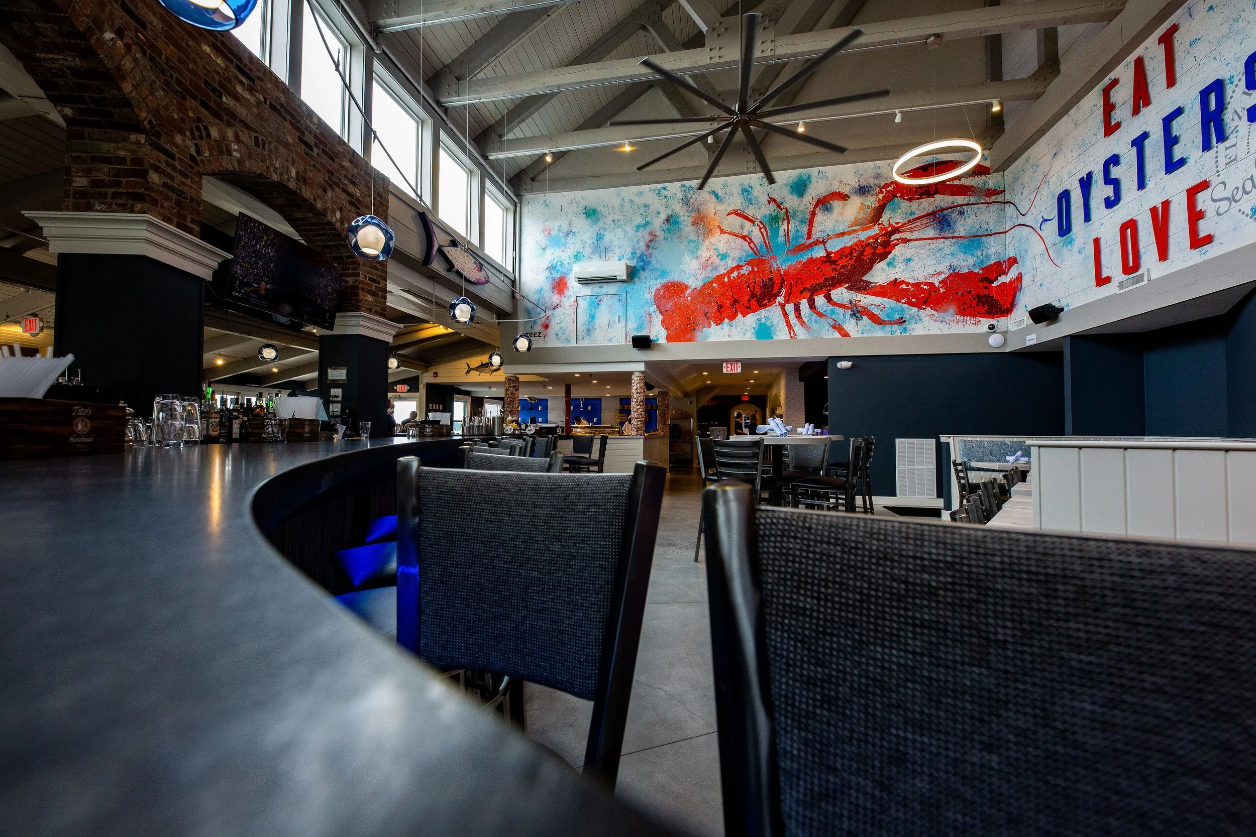 Upscale seafood restaurant interior with bar seating, dining tables, nautical decor, and a large red lobster mural