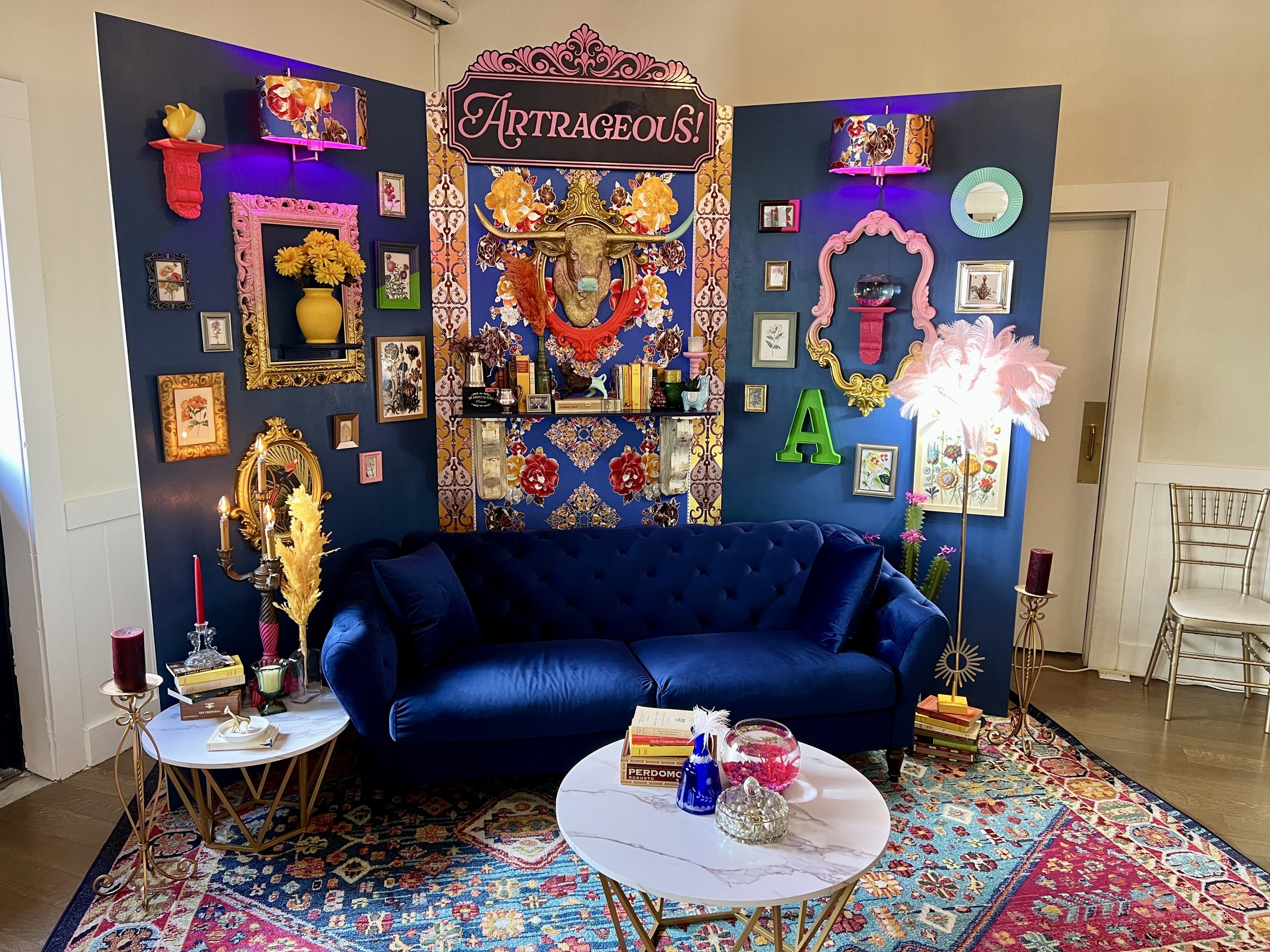 Eclectic maximalist living room with navy walls, blue velvet sofa, colorful patterned rug, floral artwork, ornate mirrors, and a decorative bull head centerpiece.