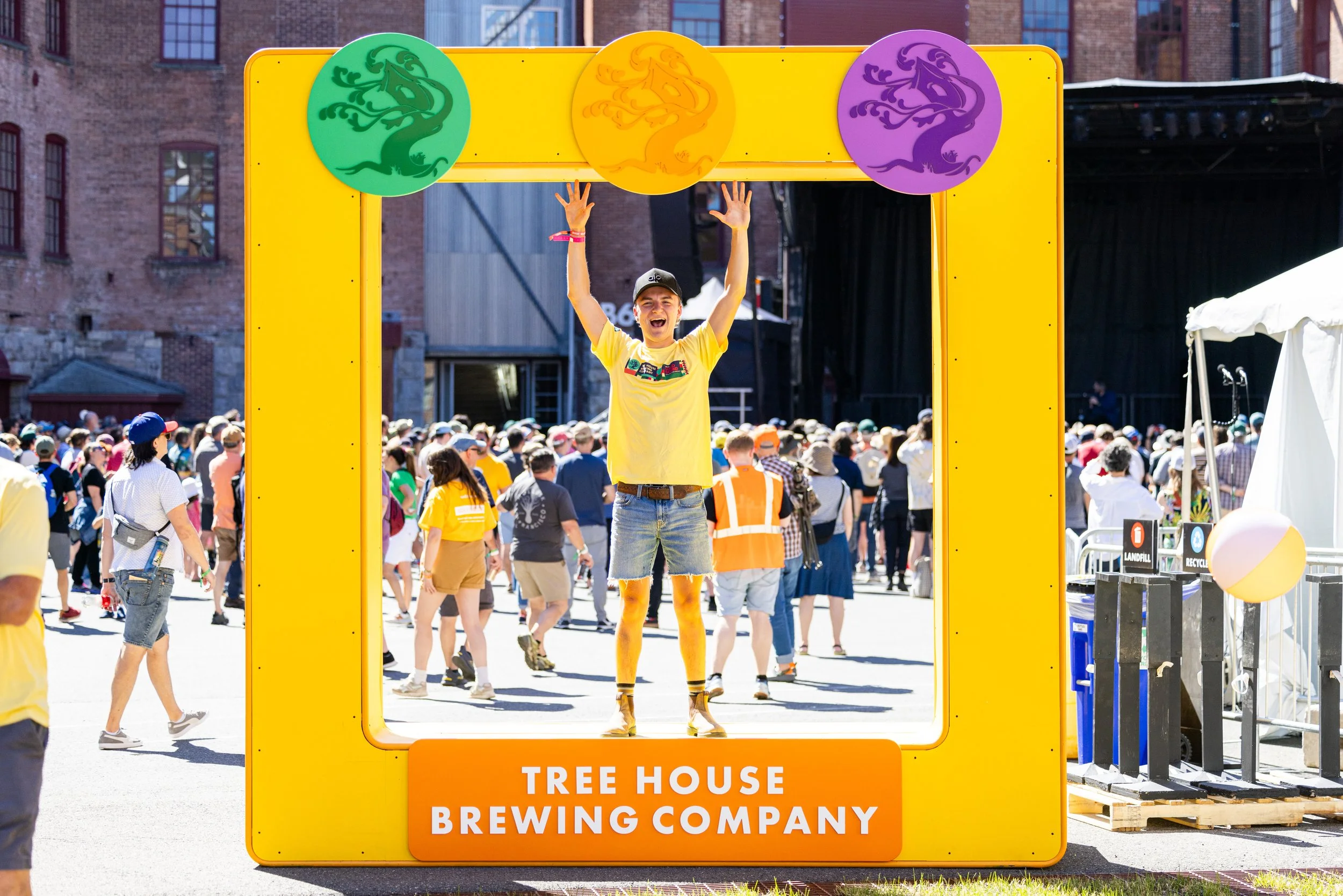Man celebrating with raised arms inside a Tree House Brewing Company photo frame at an outdoor festival