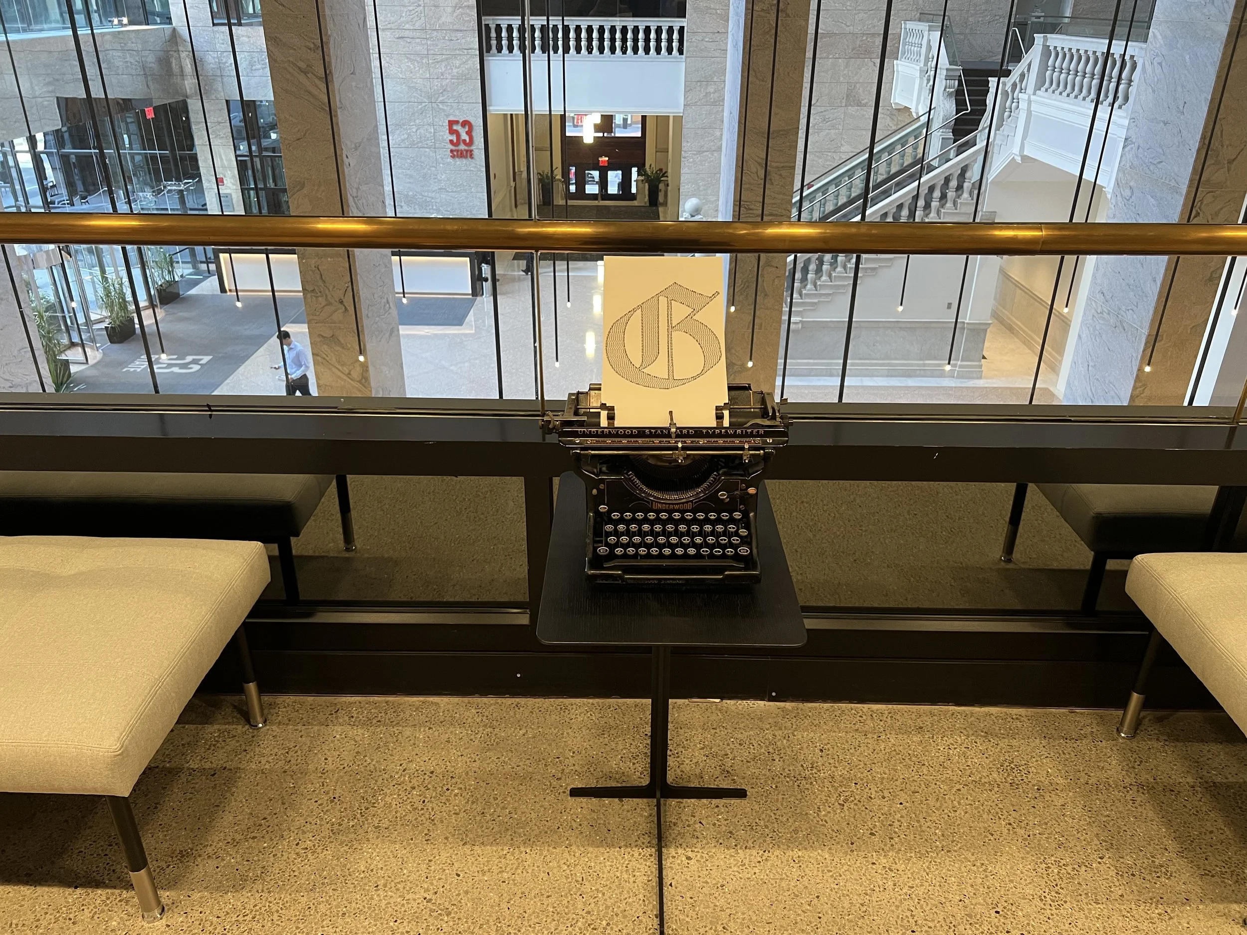Vintage Underwood typewriter displaying a sheet of paper in a modern marble atrium with a grand staircase and mirrored walls.
