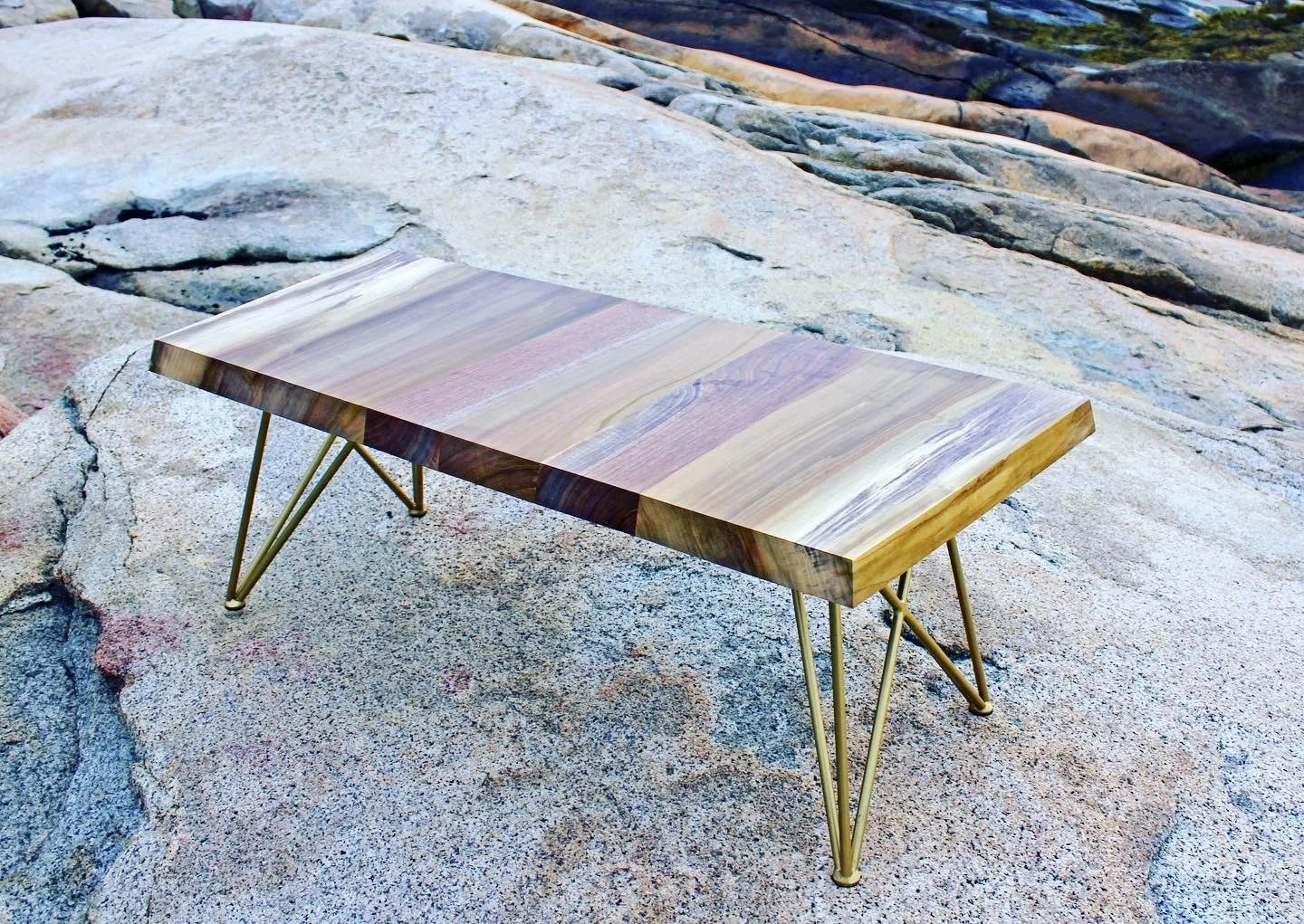 Live-edge wood coffee table with brass hairpin legs on a rocky outdoor surface