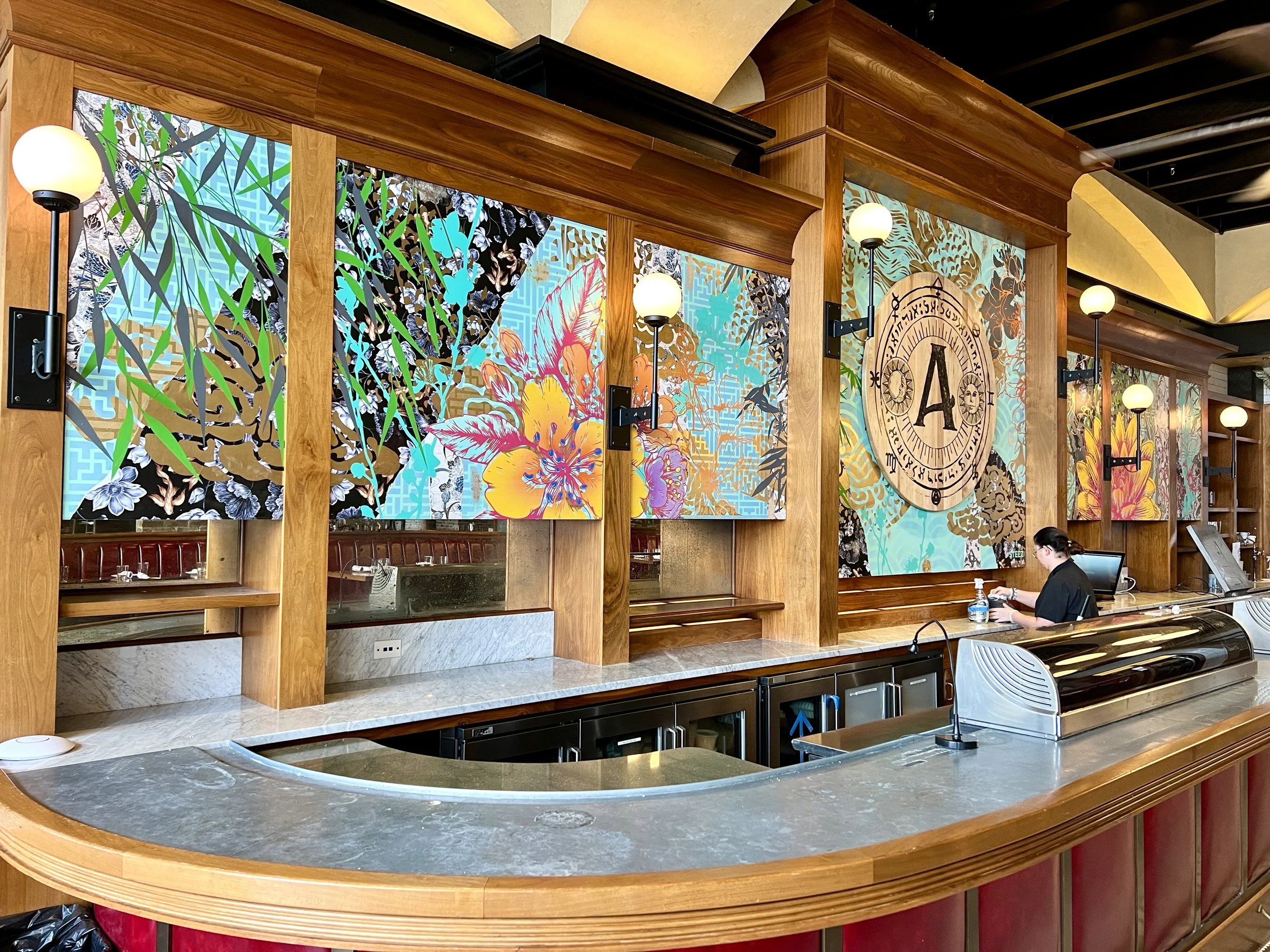 Colorful floral artwork and globe lamps decorate the wood-paneled interior of a restaurant bar.