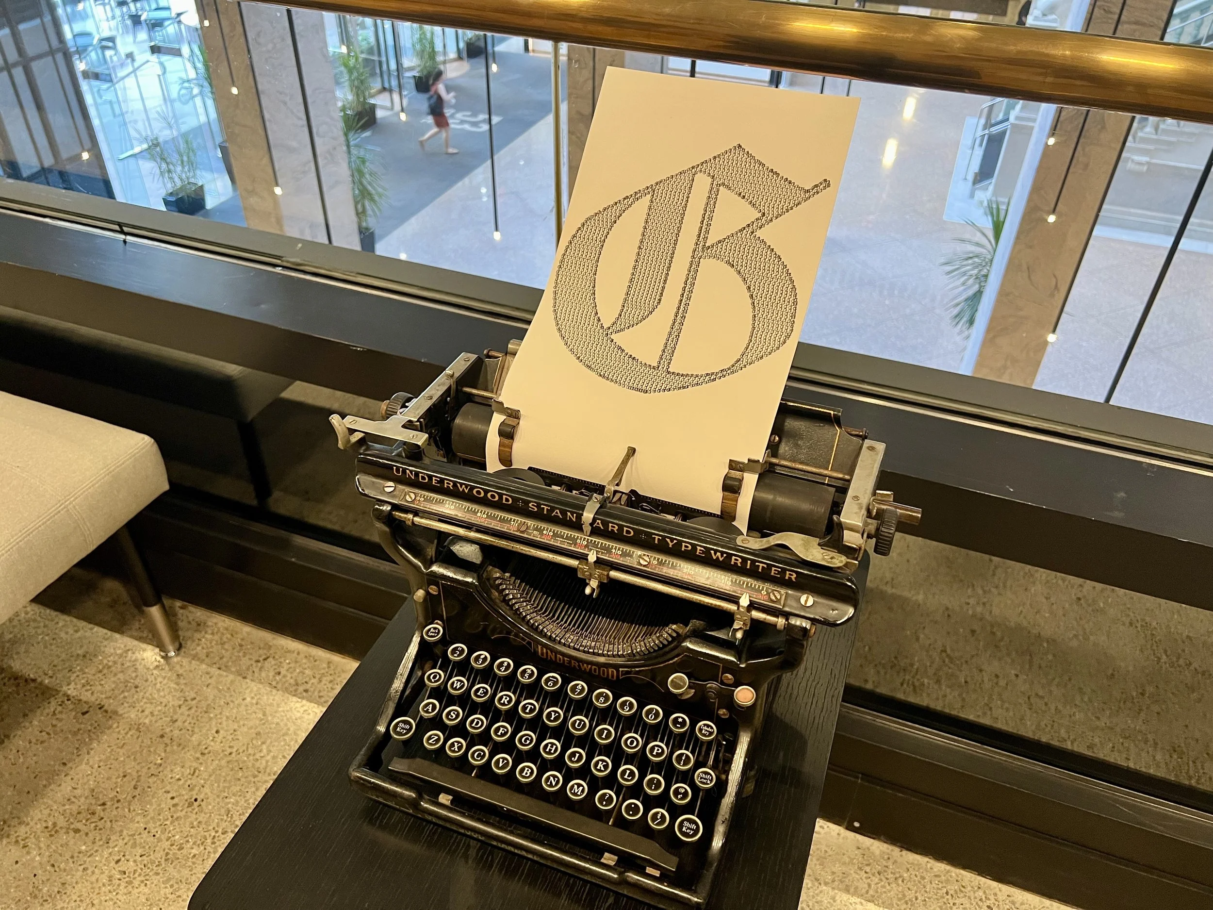 Vintage Underwood Standard typewriter displaying a large dotted letter on paper in a modern atrium