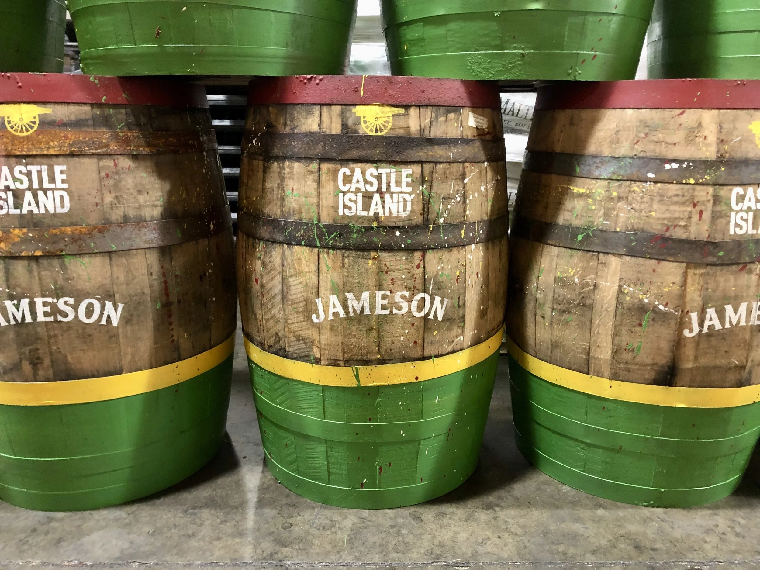 Green-and-yellow painted Jameson Castle Island whiskey barrels stacked in a distillery.