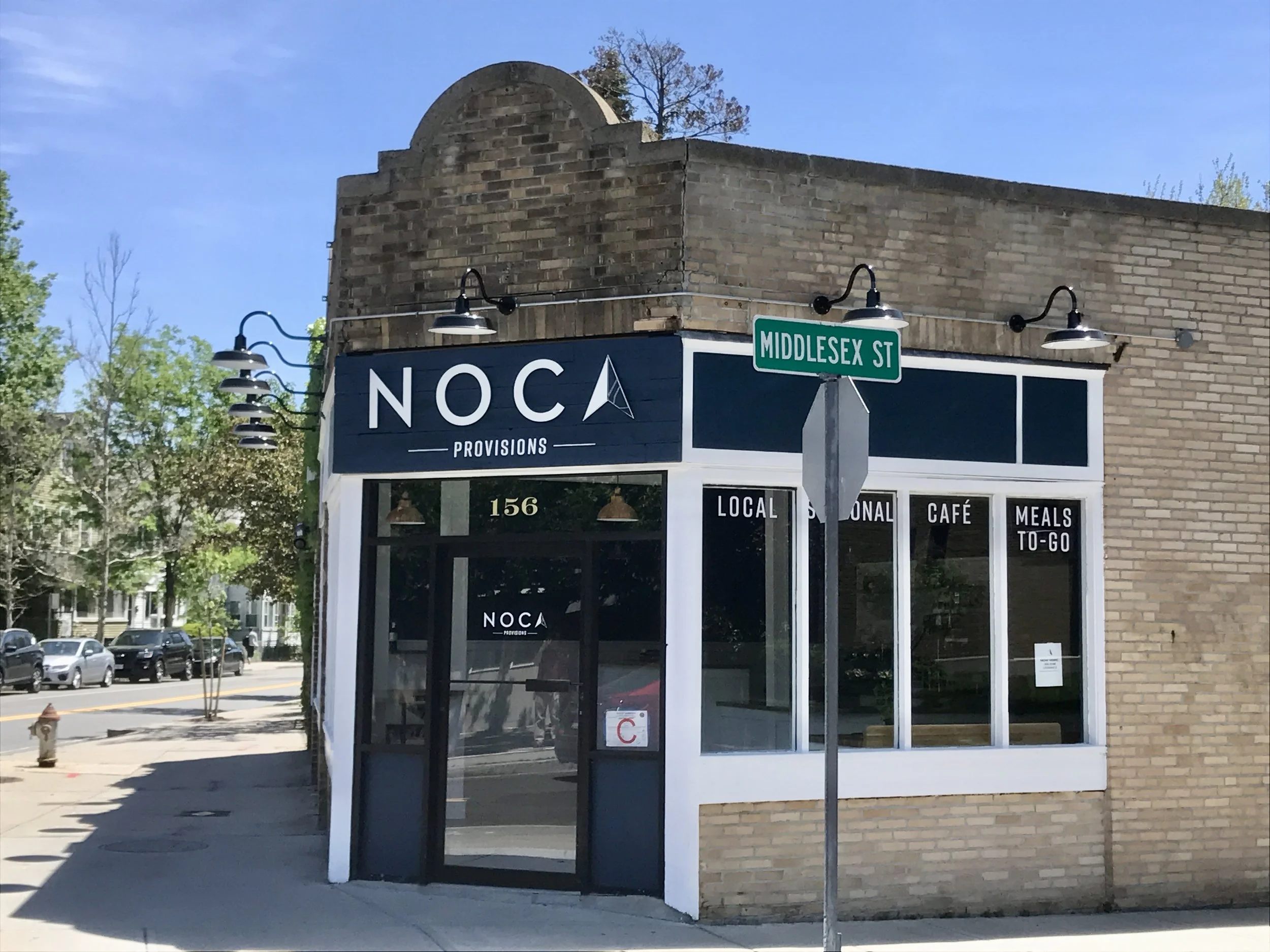 NOCA Provisions cafe storefront at 156 Middlesex Street, with a street sign, sidewalk, and parked cars.