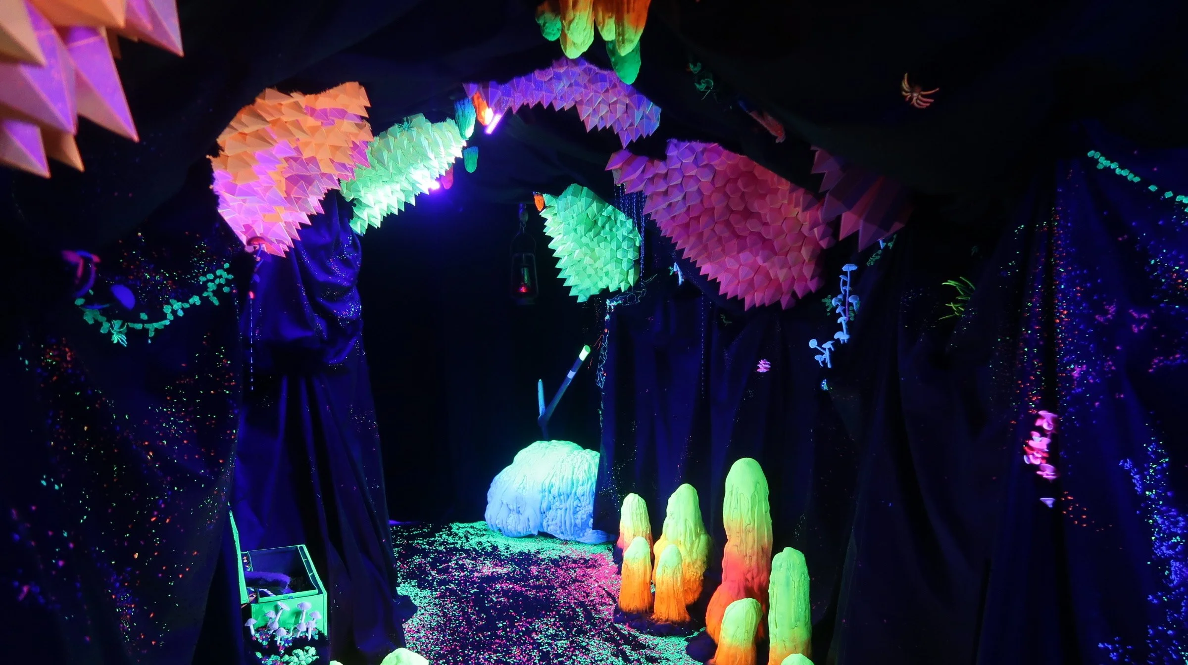 Blacklight-lit fantasy forest display with colorful hanging leaves, glowing mushrooms, glittering plants, and dark tree-like structures