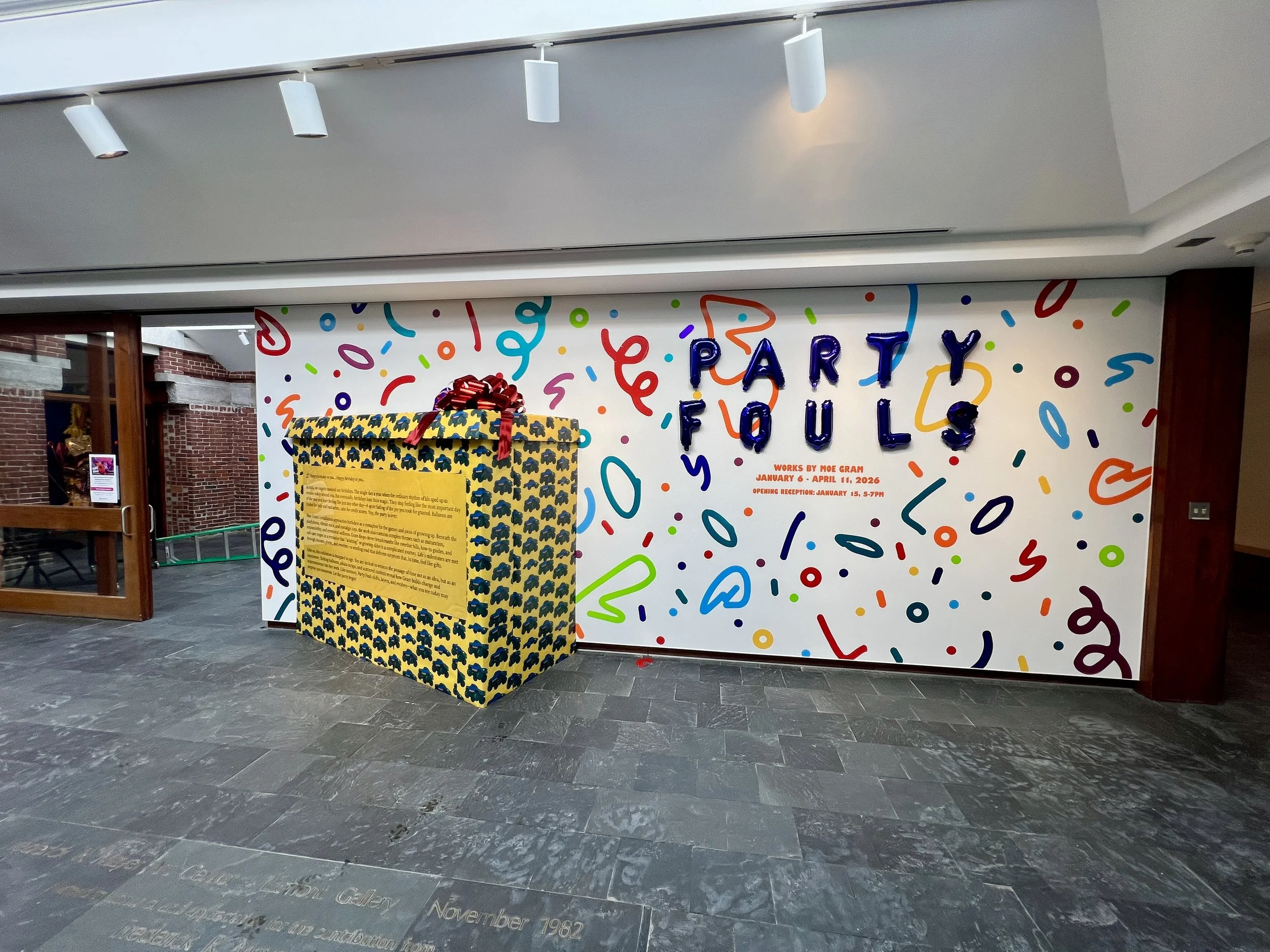 Museum gallery entrance with a colorful “PARTY FOULS” exhibition mural, confetti designs, and a large wrapped gift box.