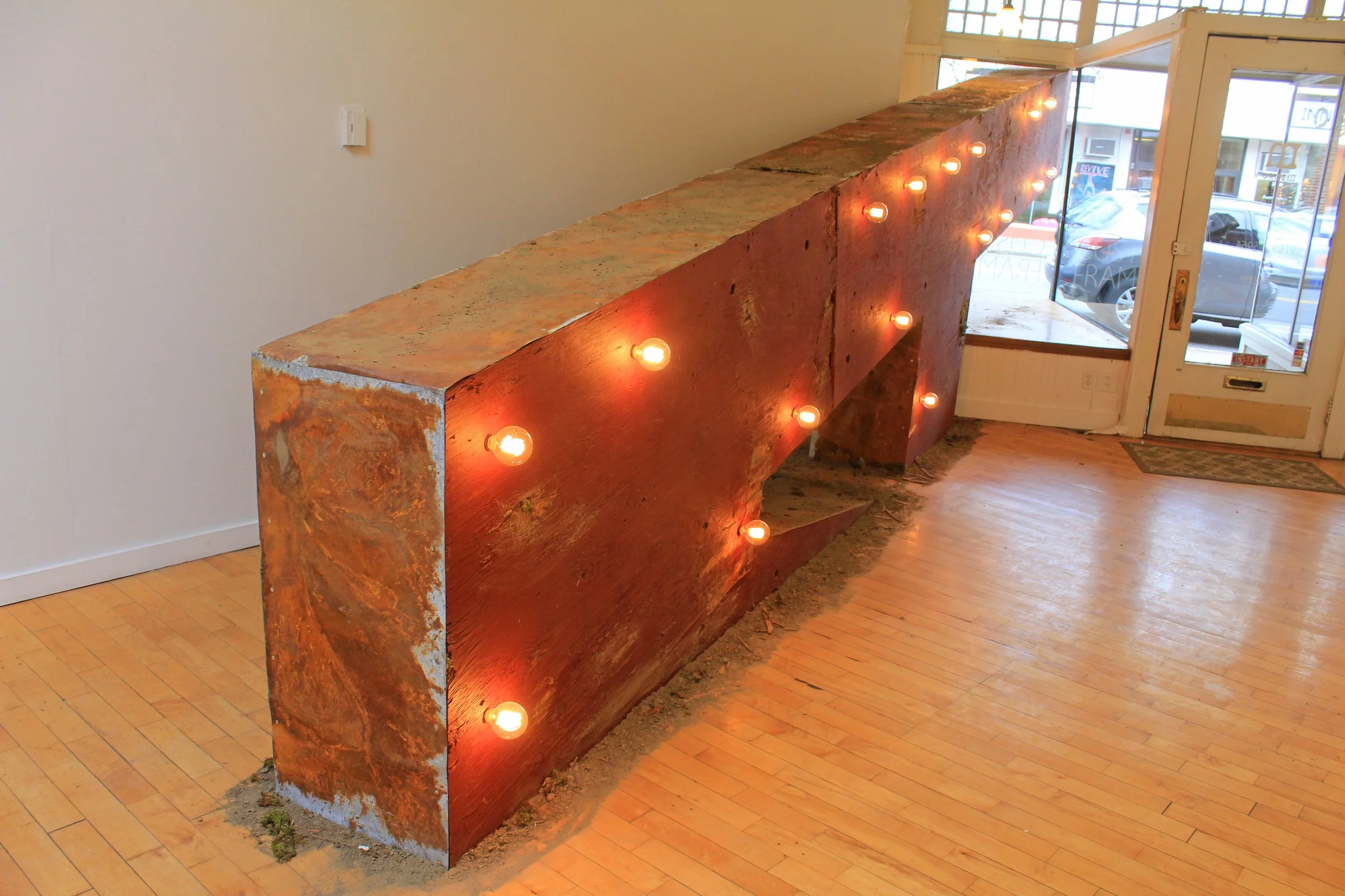 Large rustic wooden structure with glowing marquee bulbs inside a storefront.