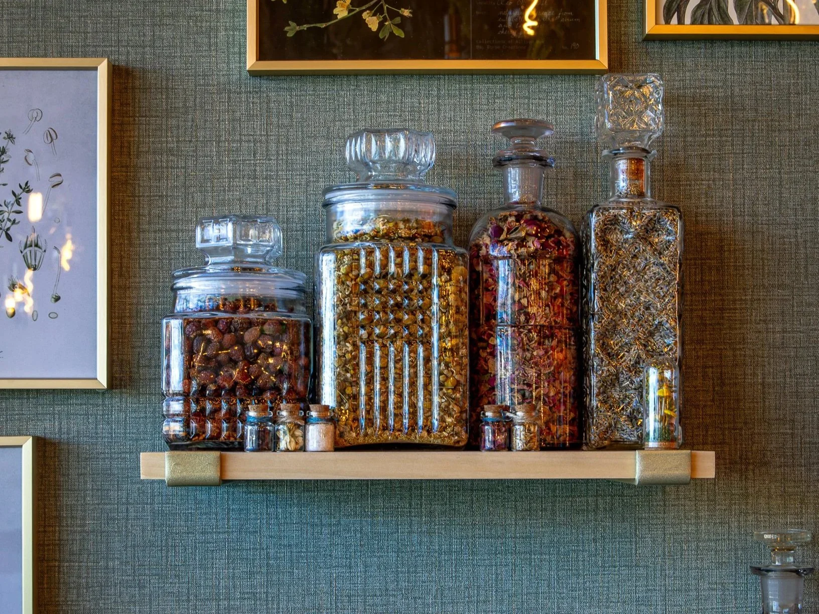 Decorative glass jars filled with dried flowers, herbs, and botanicals on a wall shelf
