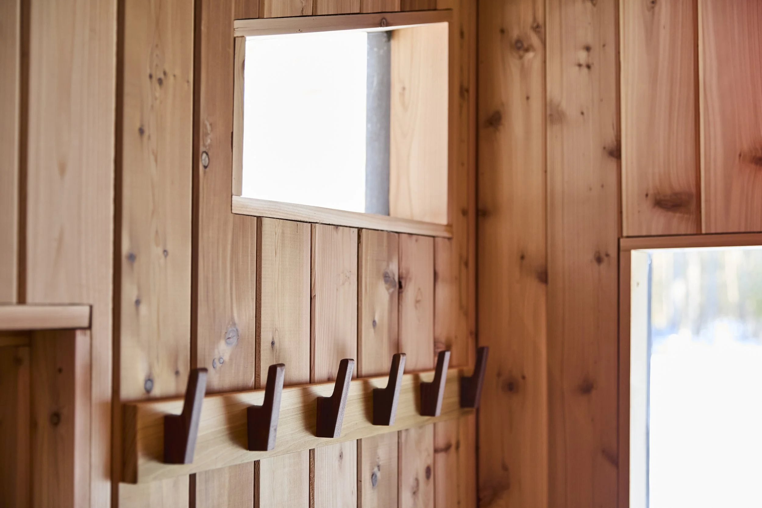 Rustic wood-paneled interior with a wall-mounted coat rack, open window, and bright natural light.