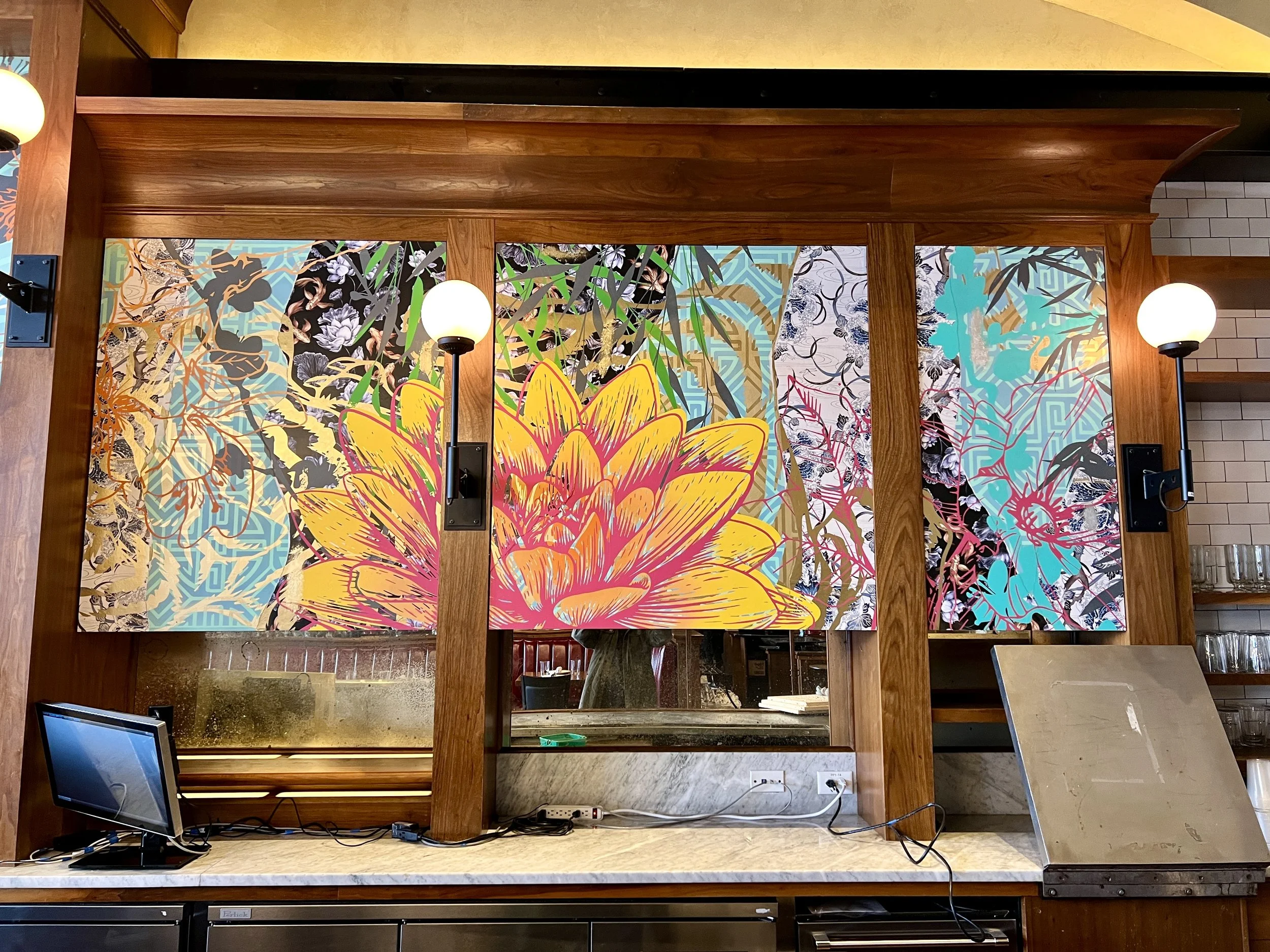 Colorful abstract floral mural behind a wood-framed restaurant bar with globe lights and marble countertop