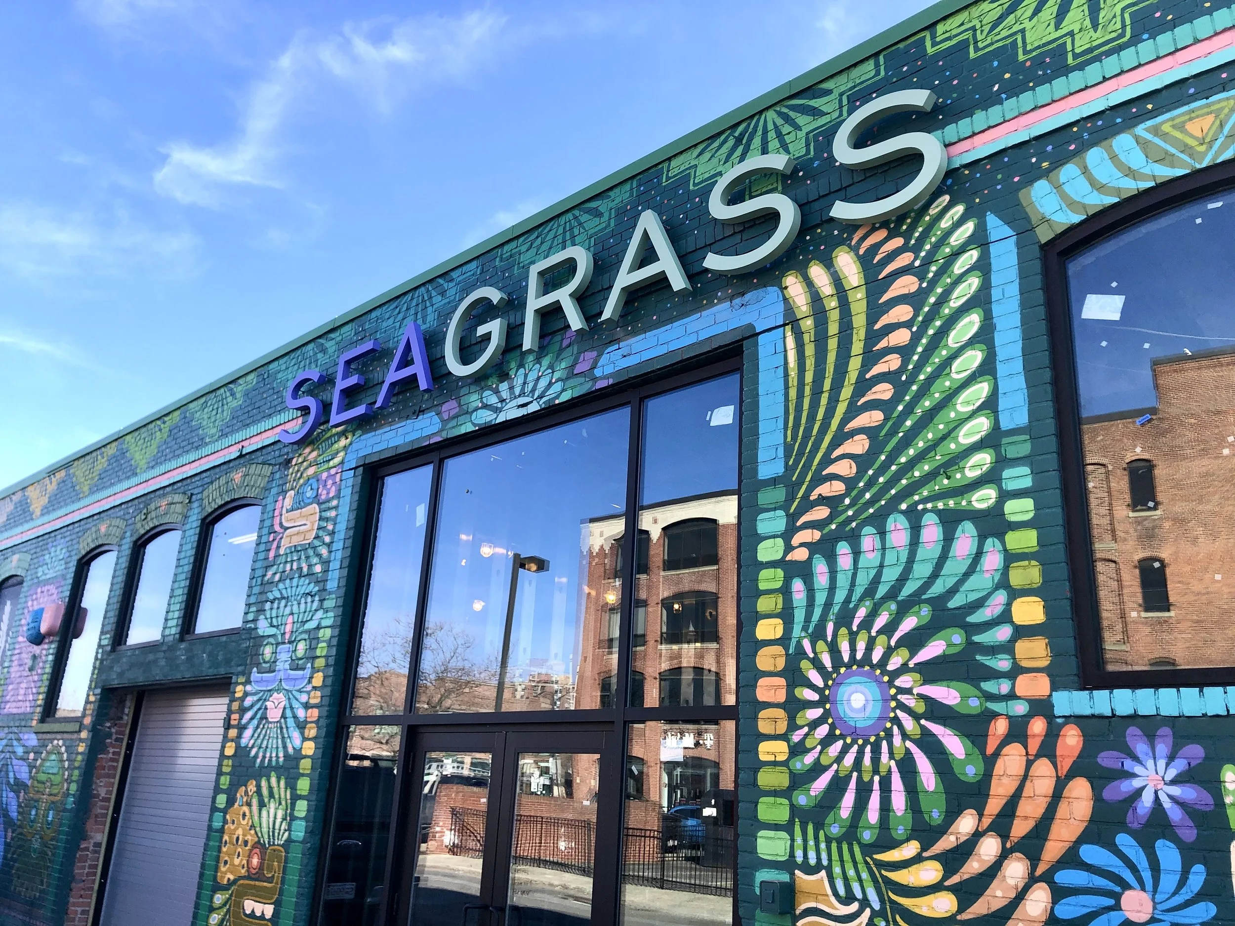 Colorful flower mural on the exterior of a building with large “SEA GRA$$” signage and storefront windows.