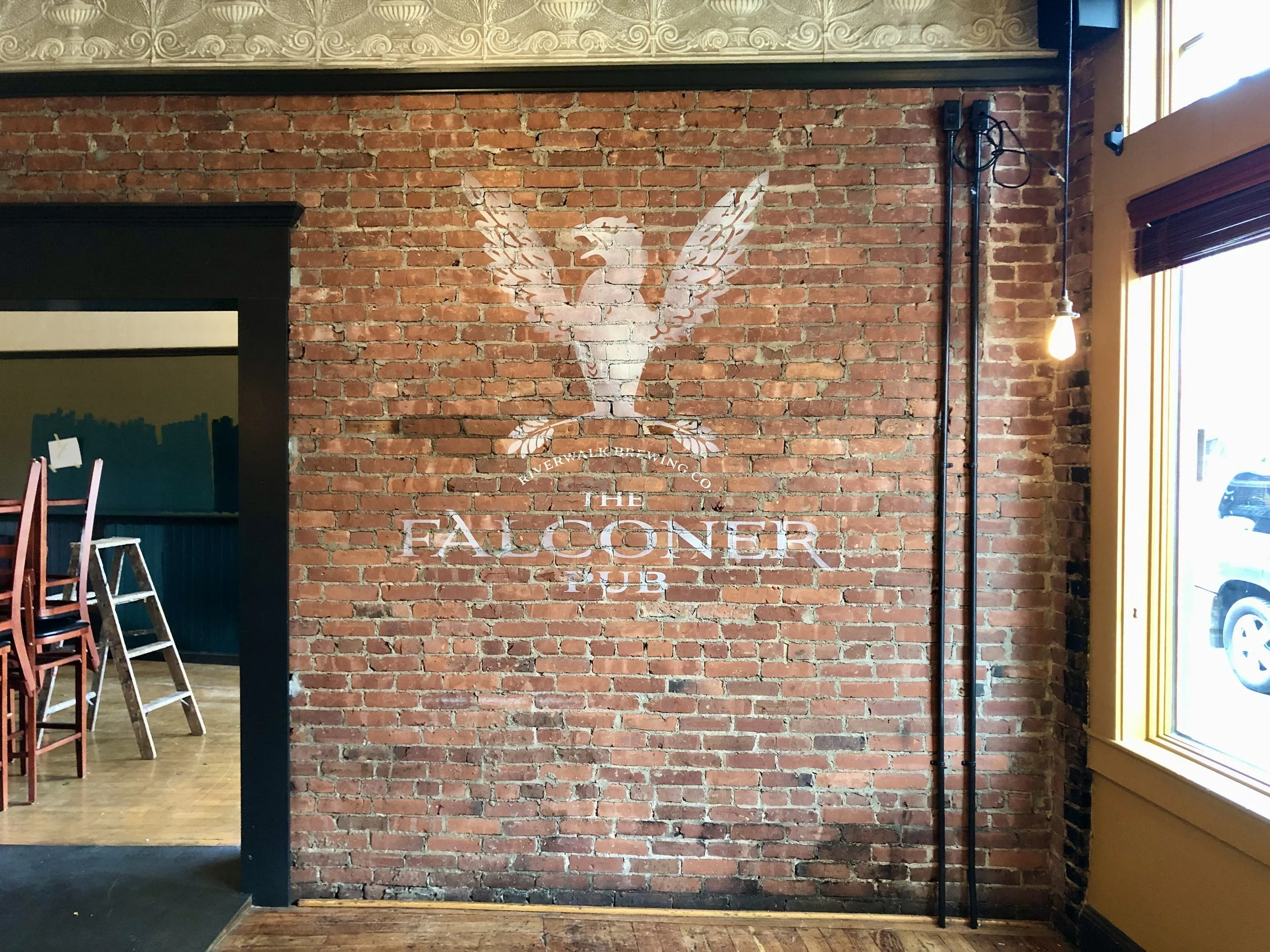 Exposed brick wall with faded Falconer Pub mural, hanging pendant light, window, and bar seating area