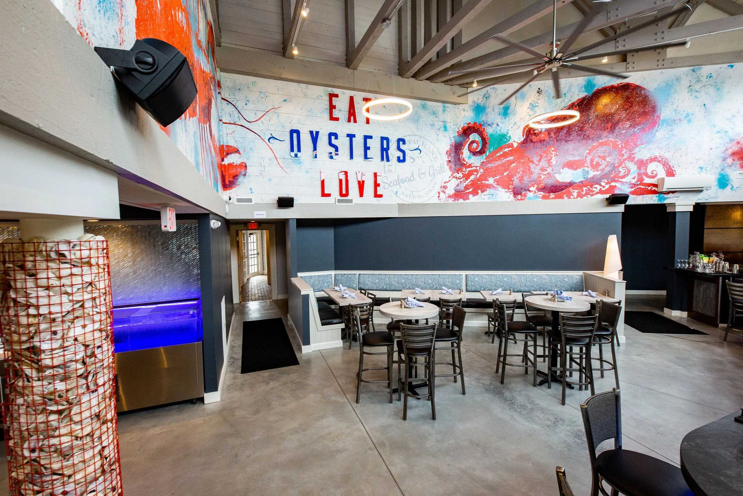 Interior of a seafood restaurant featuring oyster-themed artwork, colorful octopus mural, dining tables, and booth seating