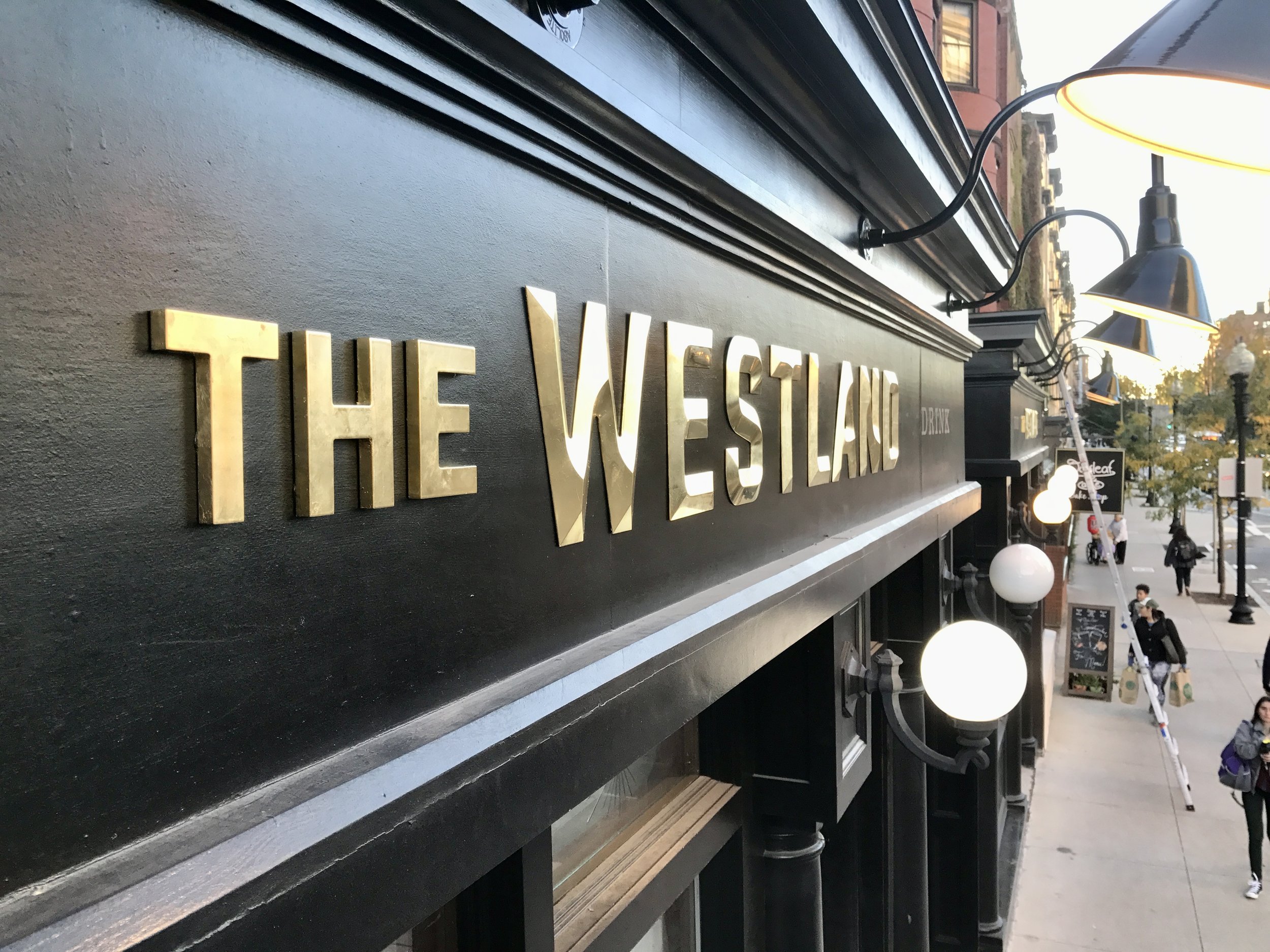 Close-up of The Westin hotel sign on a black facade with outdoor lamps and a city sidewalk