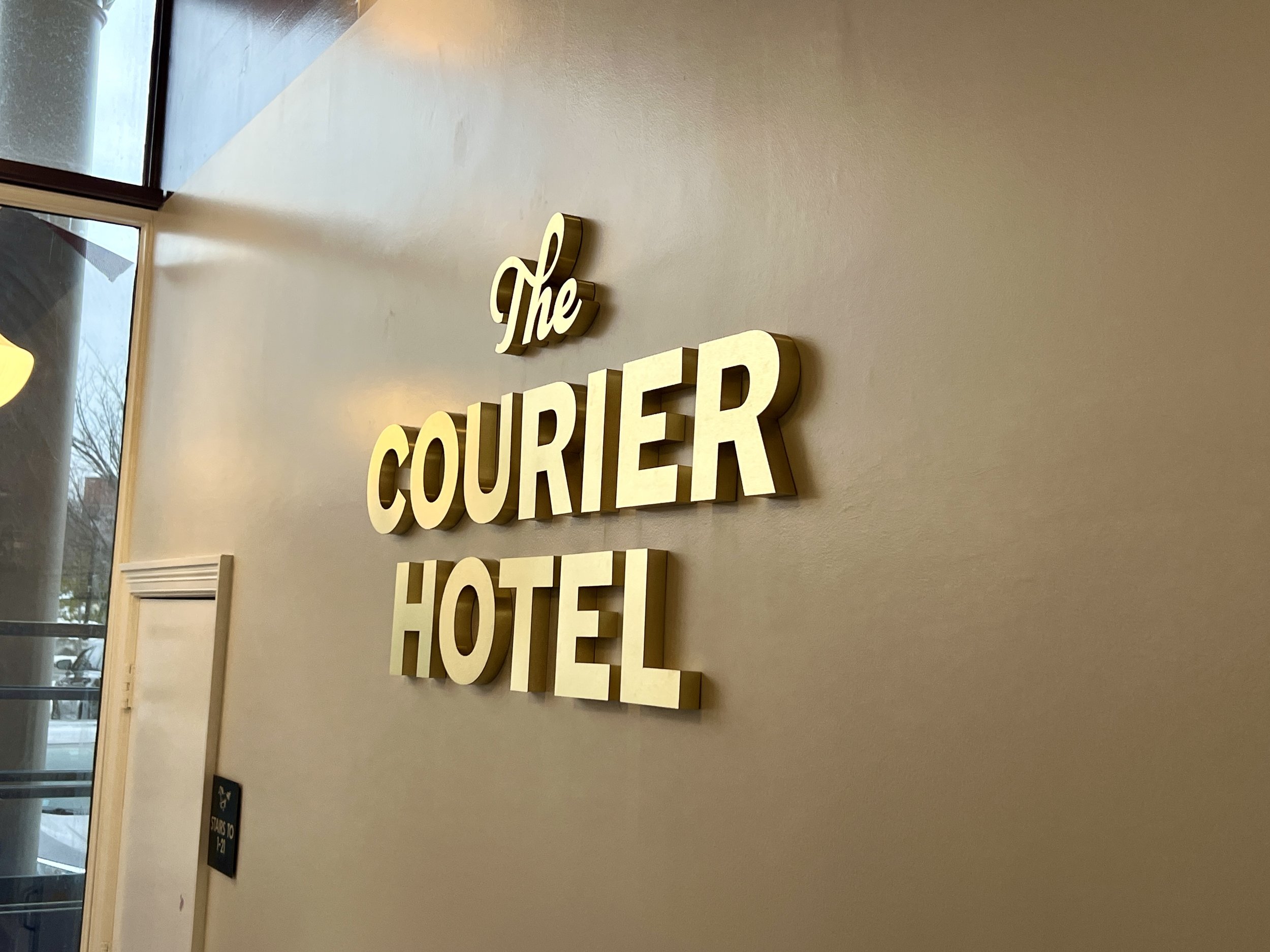 Wall-mounted gold sign reading “The Courier Hotel” beside a window.