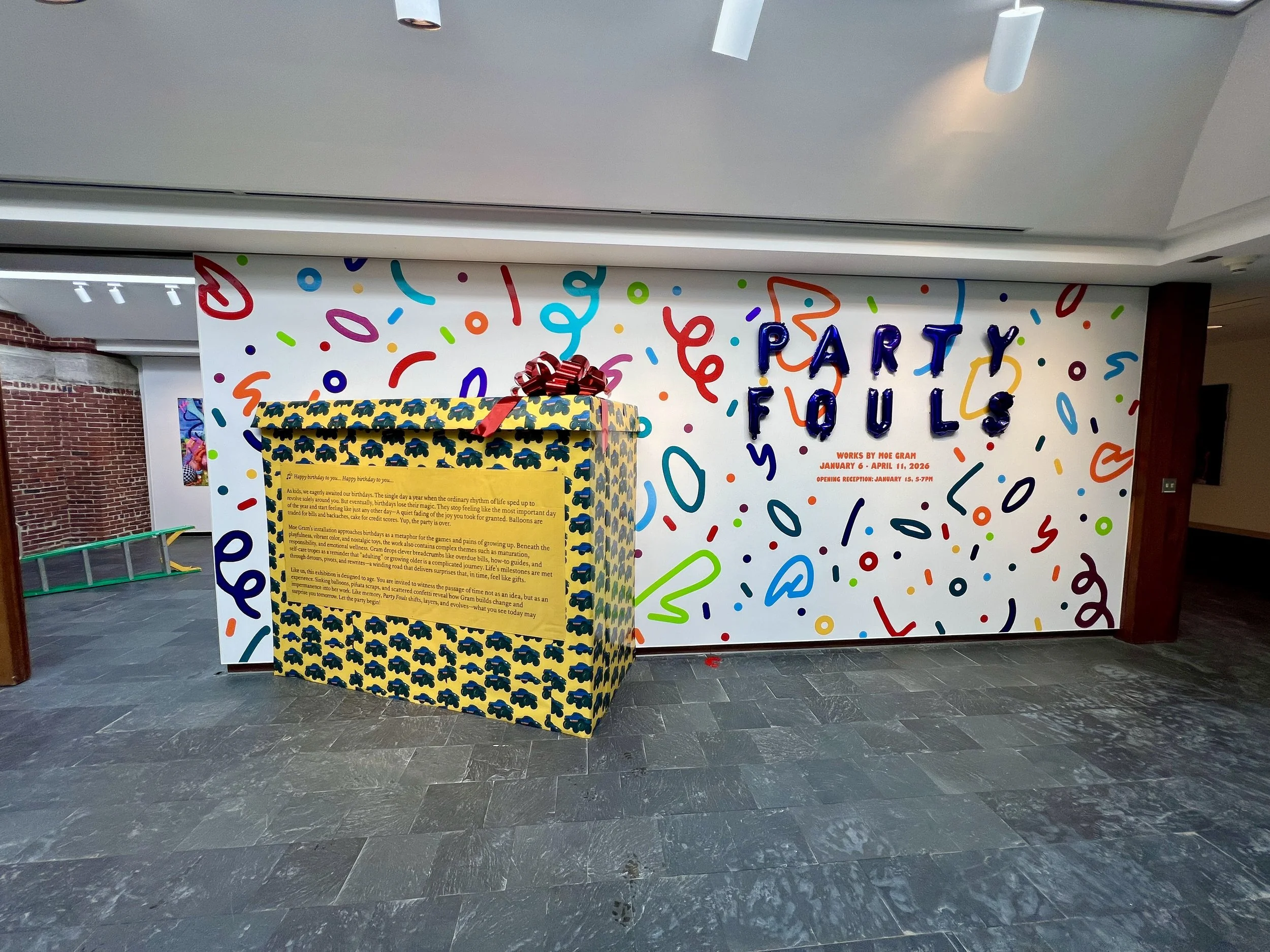 Museum exhibition featuring a giant toy-patterned birthday present and colorful wall lettering reading “Party Fowls.”