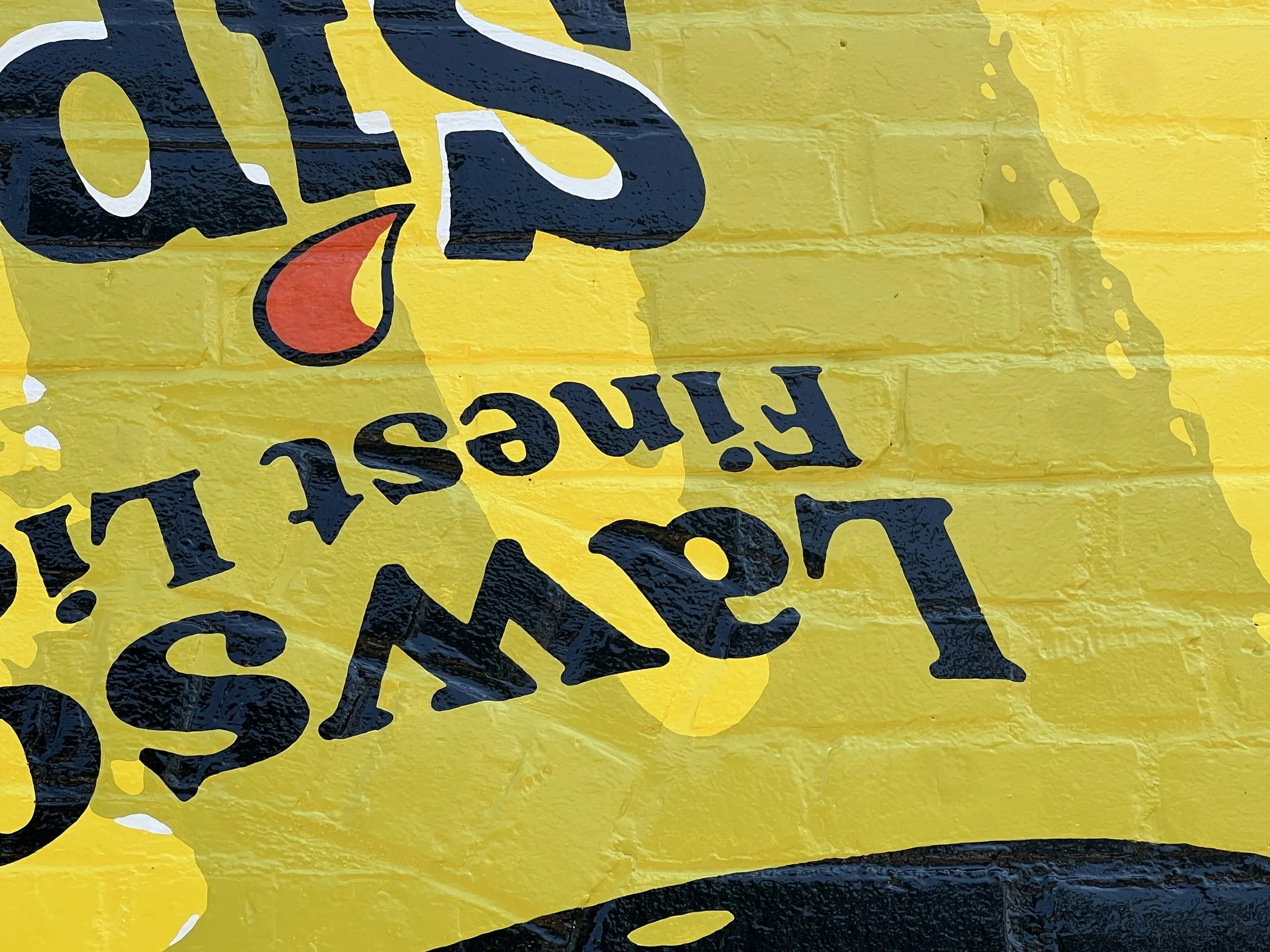 Close-up of a yellow and black painted sign with partial lettering and a red flame-like graphic