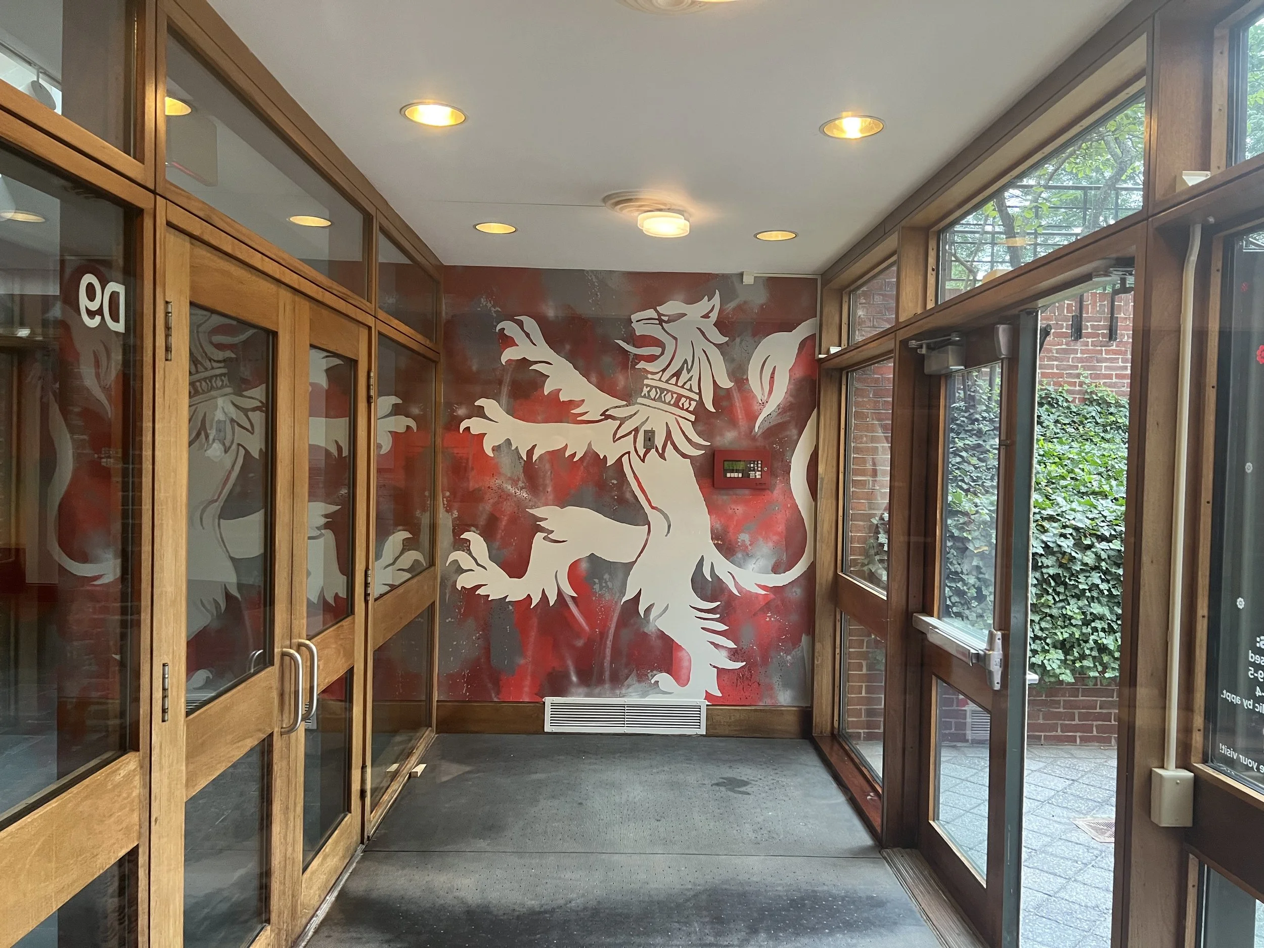 Wood-framed glass lobby with a large red-and-white dragon mural, ceiling lights, and windows overlooking greenery.