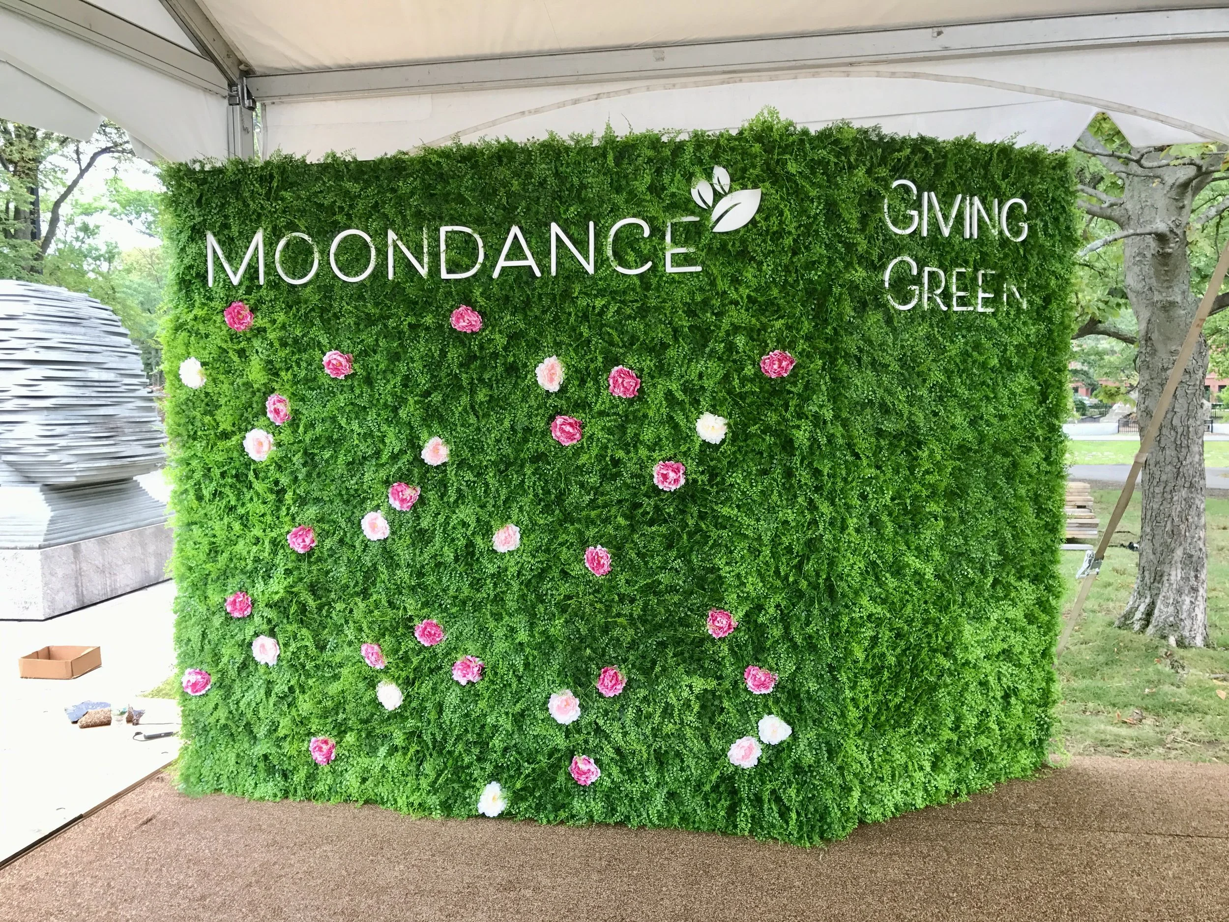 Green floral event backdrop reading “MOONDANCE” and “GIVING GREEN,” decorated with pink and white flowers.