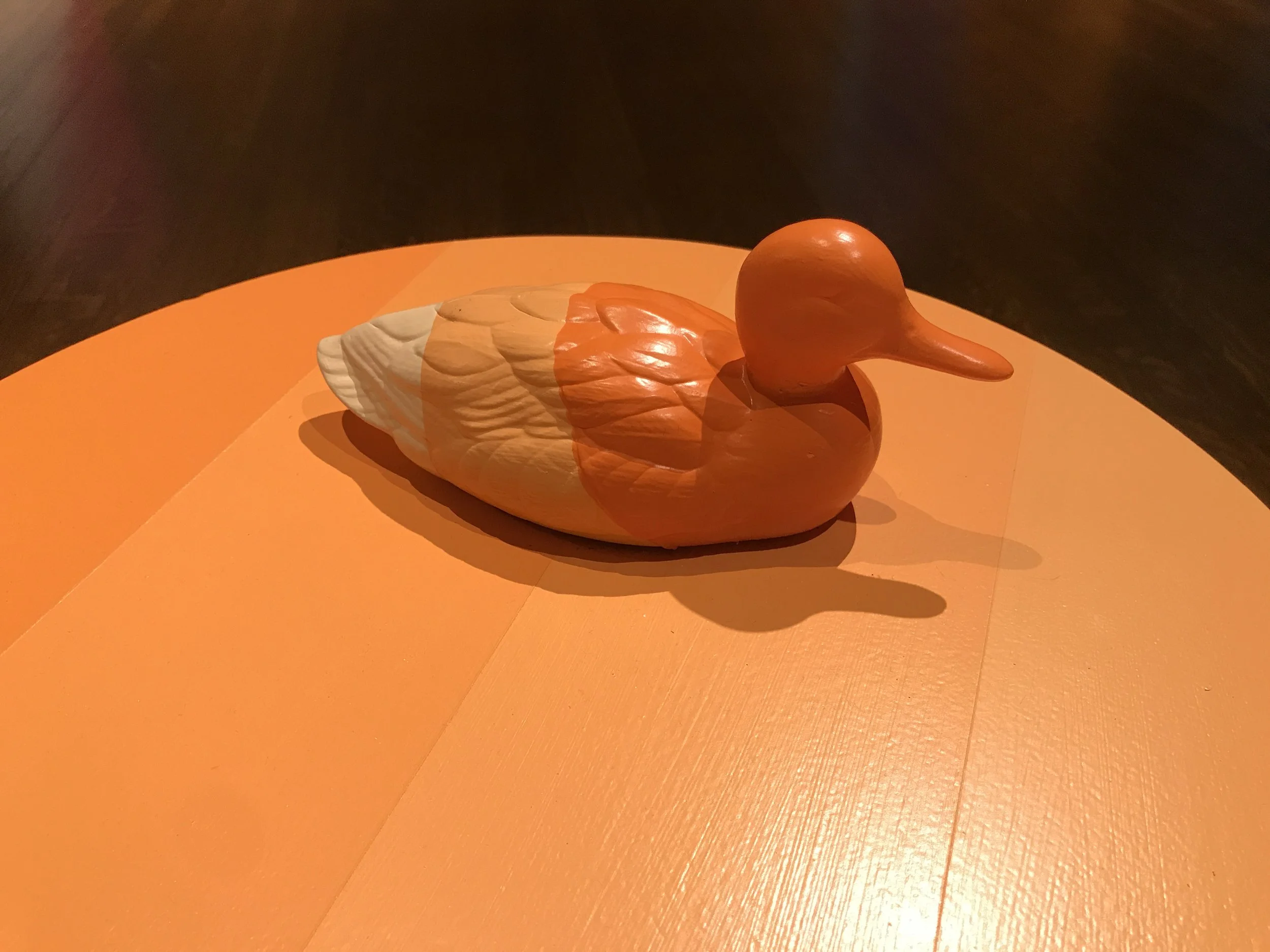 Orange and white wooden duck sculpture on an orange table.