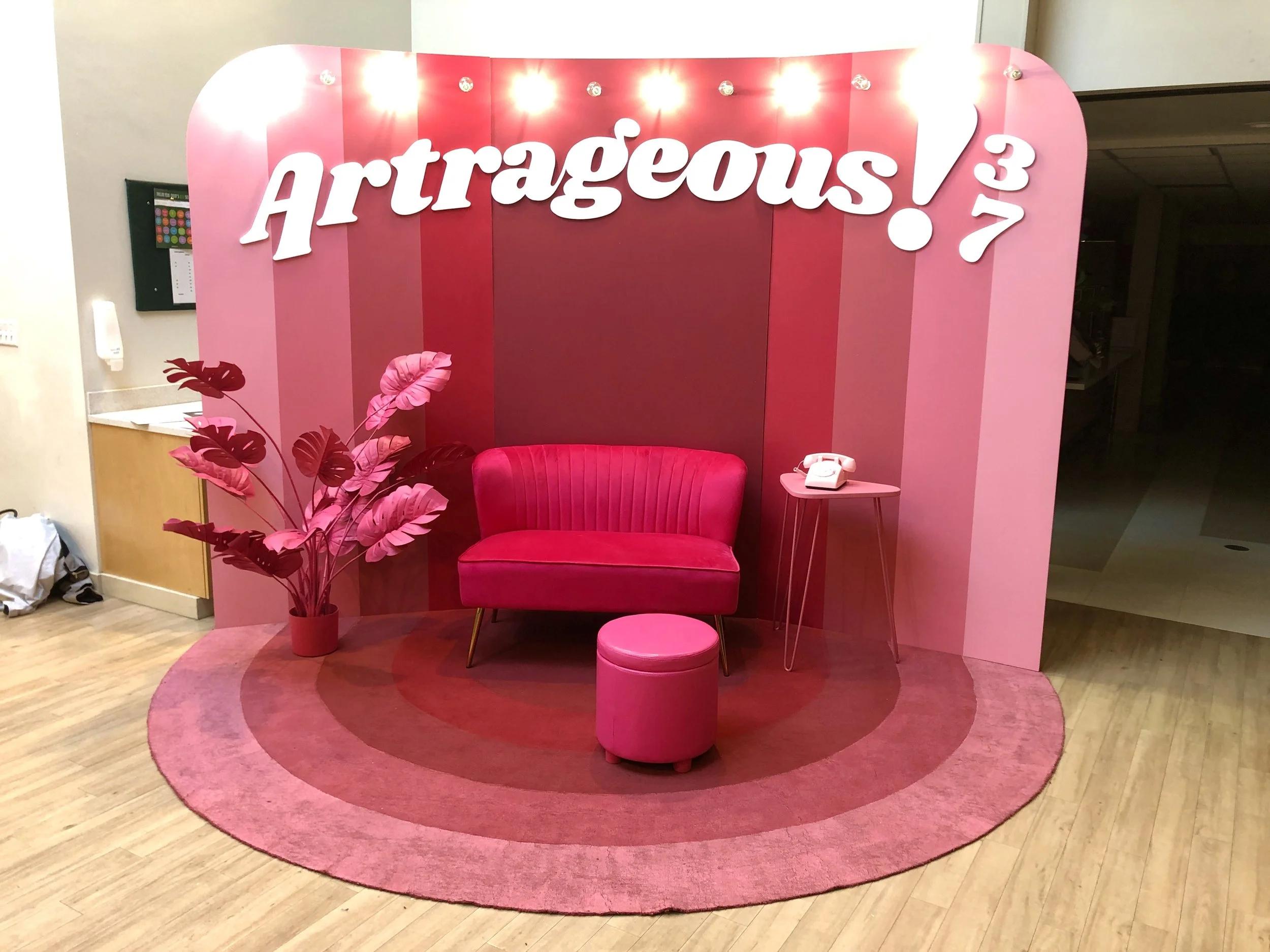 Pink ArtRaveous photo booth backdrop with a loveseat, ottoman, side table, vintage telephone, and decorative plant