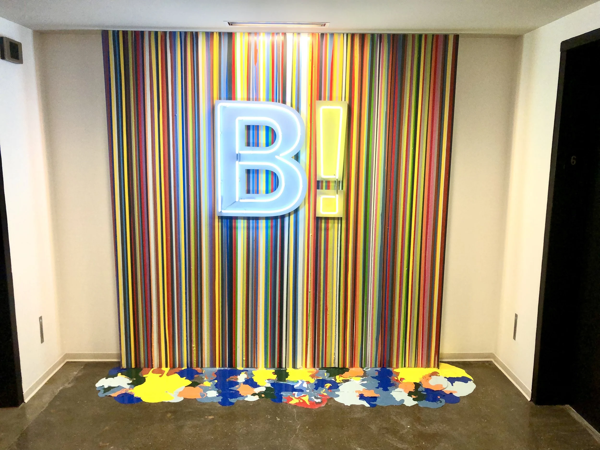 Colorful striped wall with illuminated blue and yellow letters and a multicolored abstract rug in a modern lobby