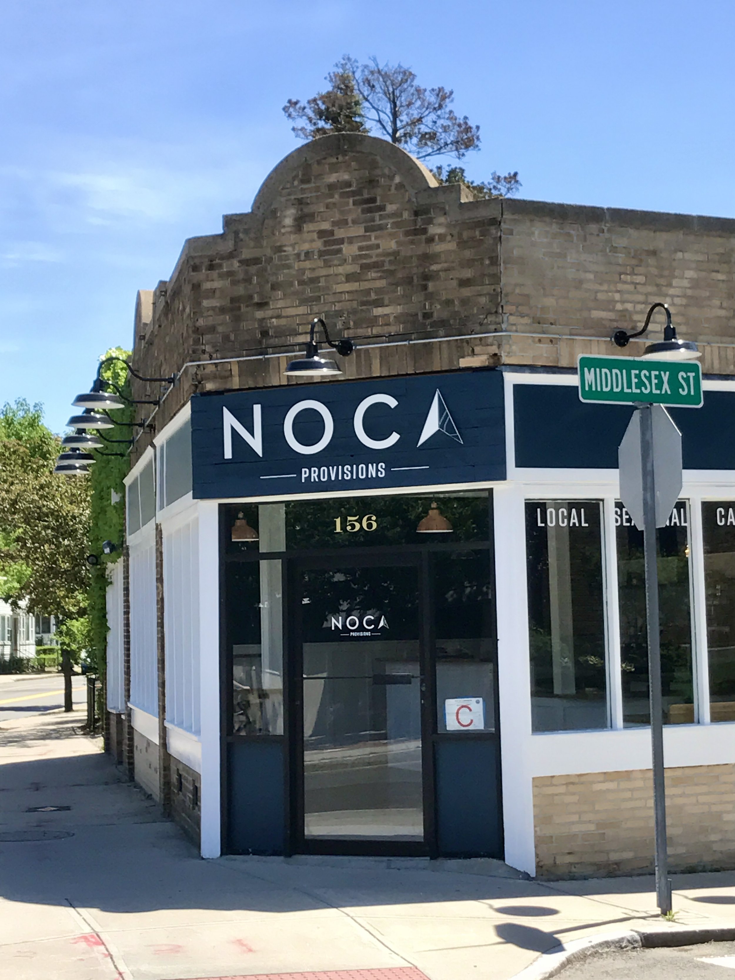 Noca Provisions storefront at 156 Middlesex Street, featuring a green Middlesex St street sign and brick building.