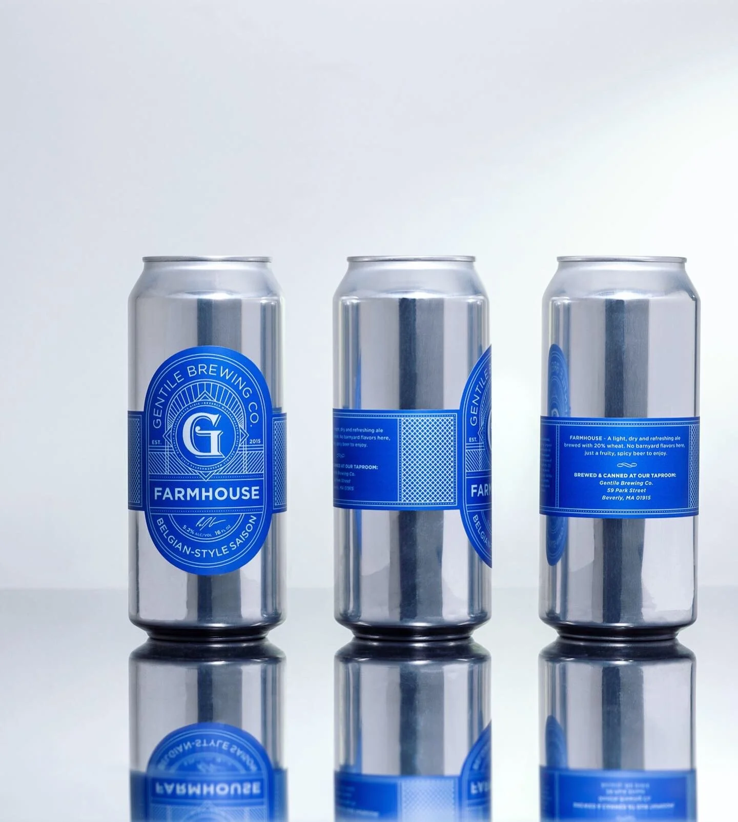 Three silver cans of Gentle Brewing Co. Farmhouse Belgian-style saison beer with blue labels, reflected on a glossy surface.