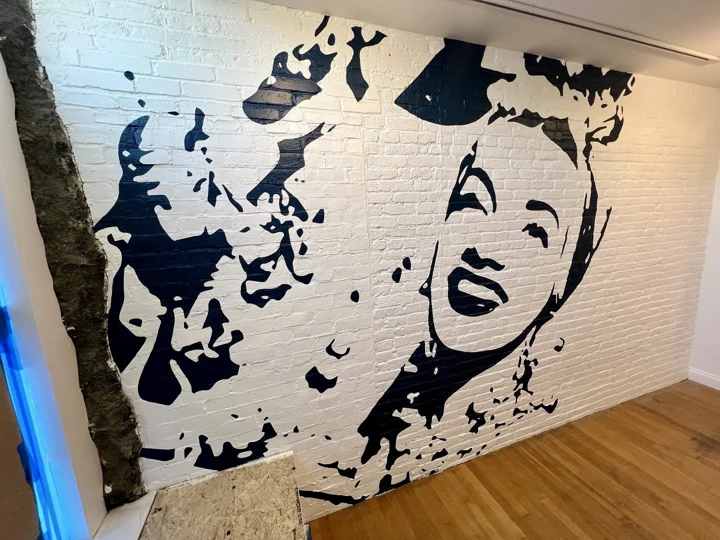 Black-and-white mural of Marilyn Monroe and James Dean on a white brick wall