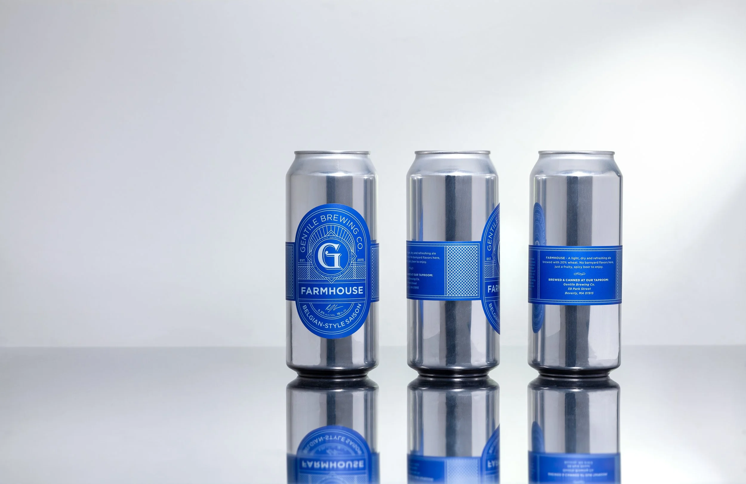 Three silver cans of Gentile Brewing Co. Farmhouse Belgian-style saison beer with blue labels, reflected on a glossy surface.