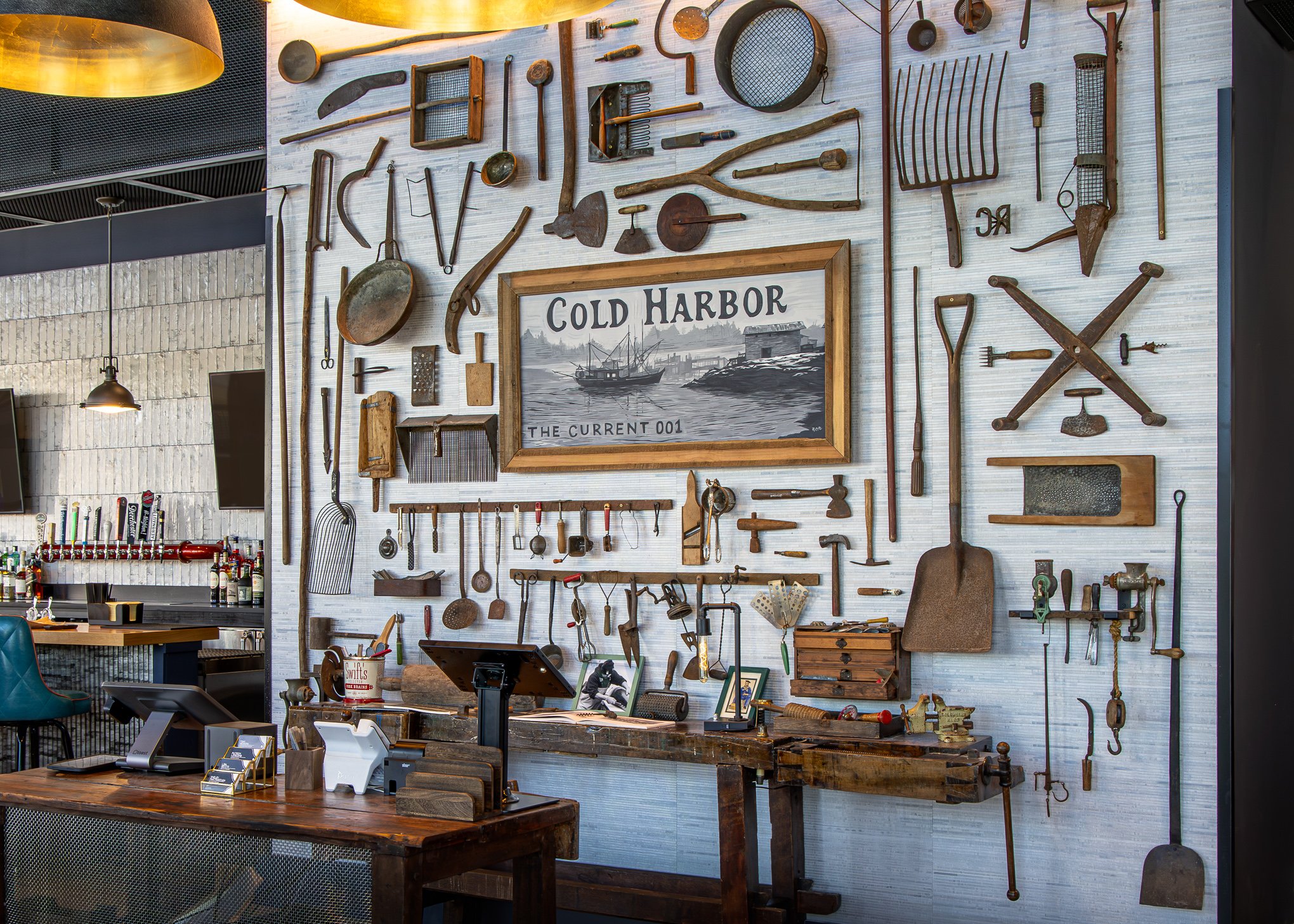Restaurant wall decorated with vintage tools, kitchen utensils, fishing gear, and a framed Cold Harbor sign above a bar counter