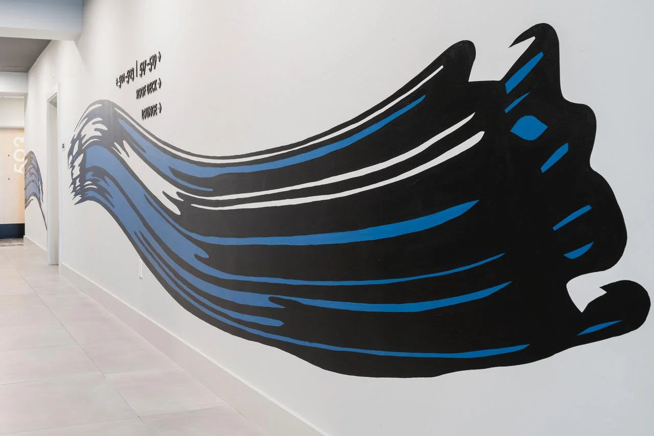 Large black and blue abstract whale mural painted on a white hallway wall
