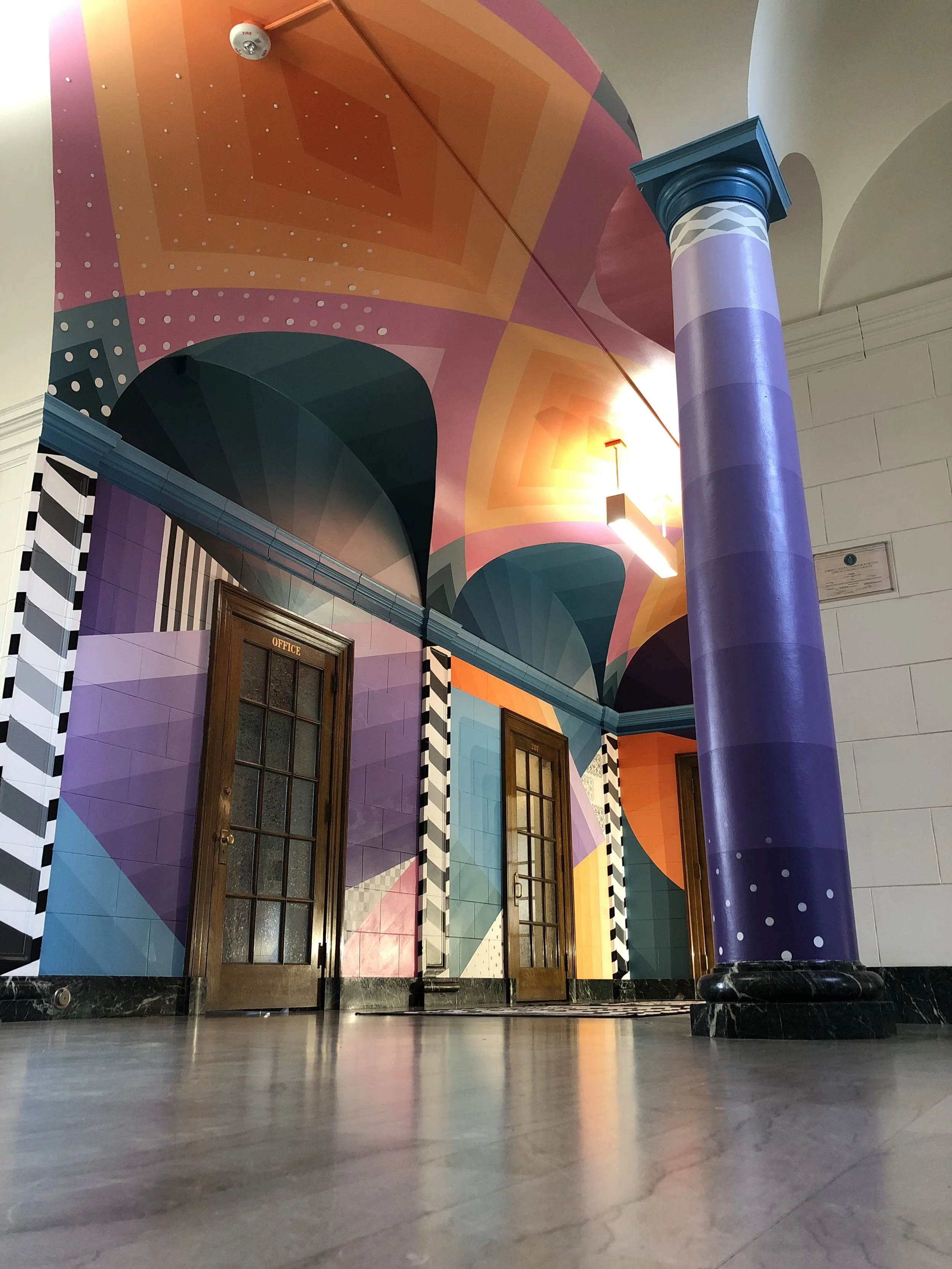 Colorful geometric Art Deco-style interior with ornate doors, purple column, patterned walls, and polished marble floor