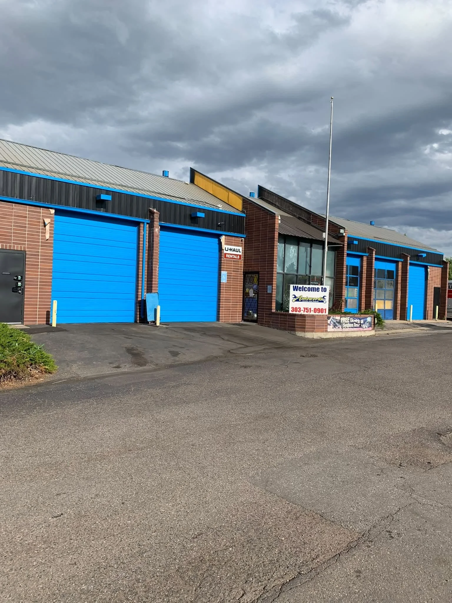 A commercial building with blue garage doors, brick walls, and a sign that says 'Welcome to Autobahn.' The building has a gray metal roof, and the sky above is cloudy with dark gray clouds.